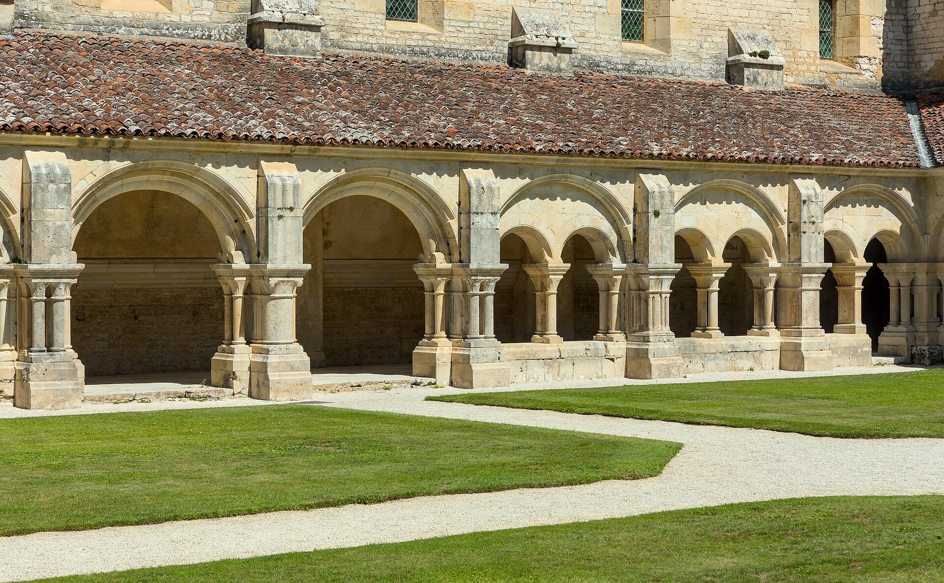 Galerie du cloître roman de Fontenay : arcades en plein cintre retombant sur des colonnes jumelles à chapiteaux, sous un toit de tuiles, ouvrant sur le jardin central engazonné