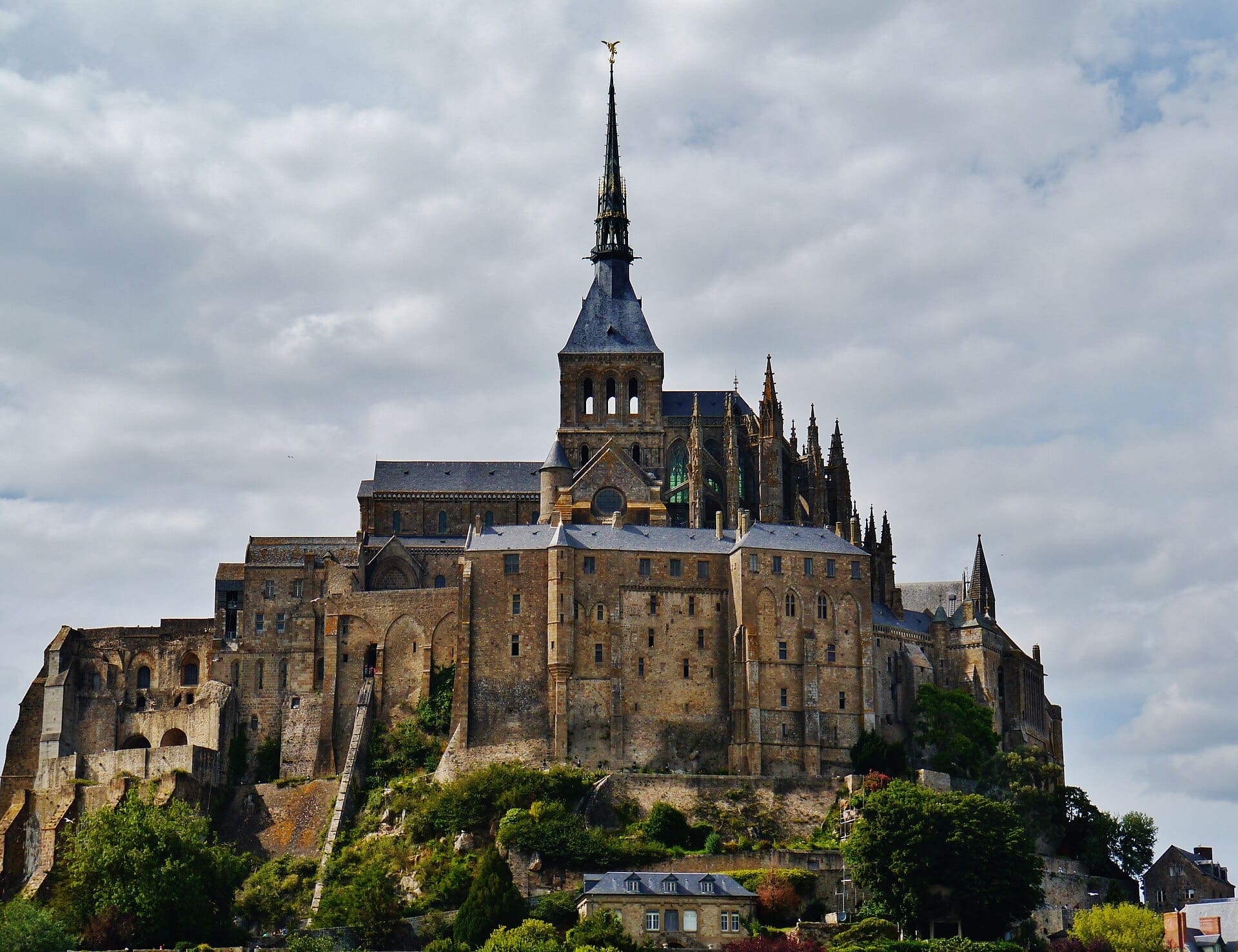 L’abbaye du Mont-Saint-Michel couronnant le rocher : flèche néogothique surmontée de la statue dorée de l’archange, chevet gothique à arcs-boutants, hauts soubassements de granit