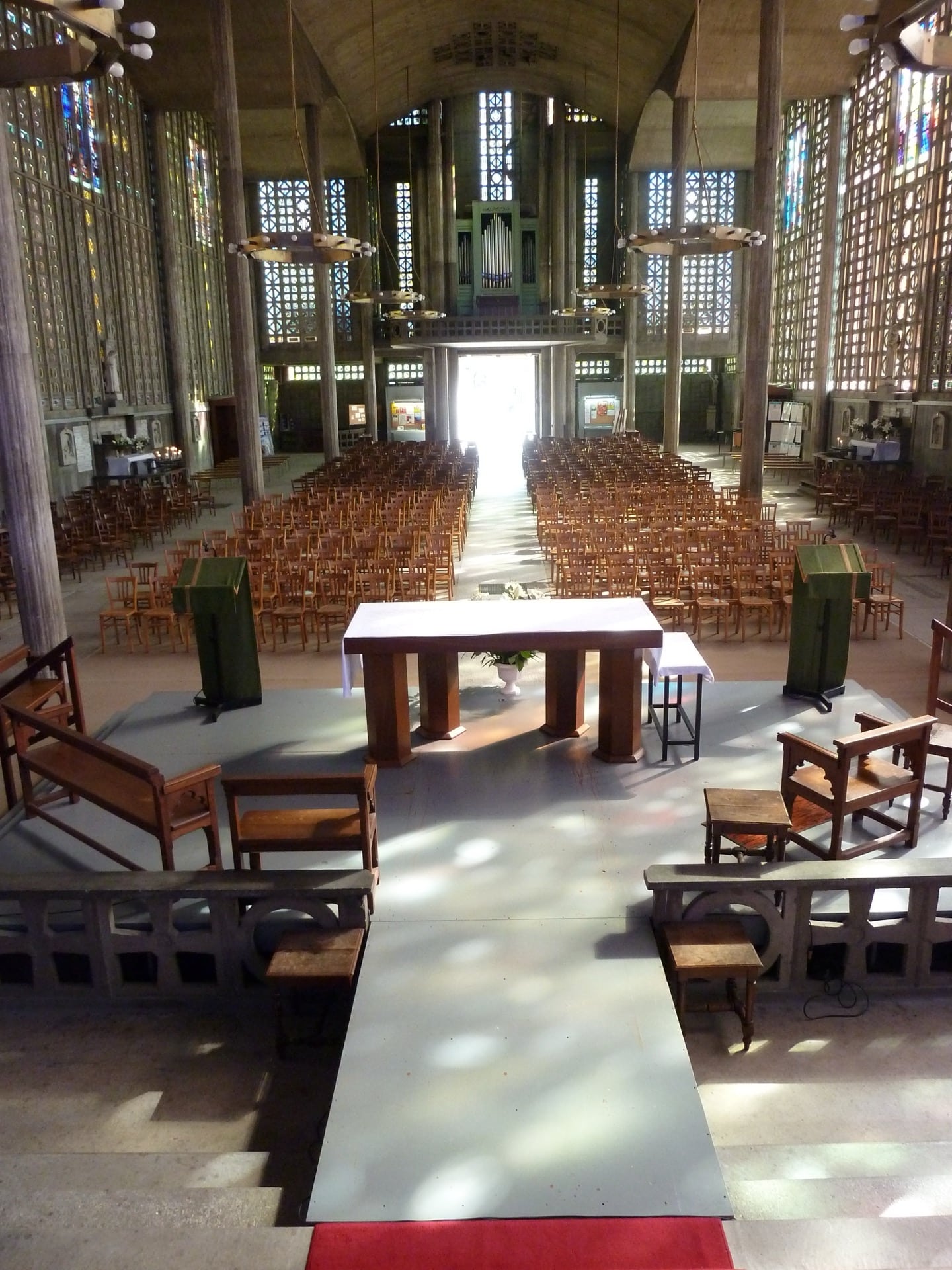 L’intérieur de l’église Notre-Dame du Raincy : nef de béton armé à fins poteaux, voûte en berceau, murs de claustras ajourés garnis de vitraux colorés