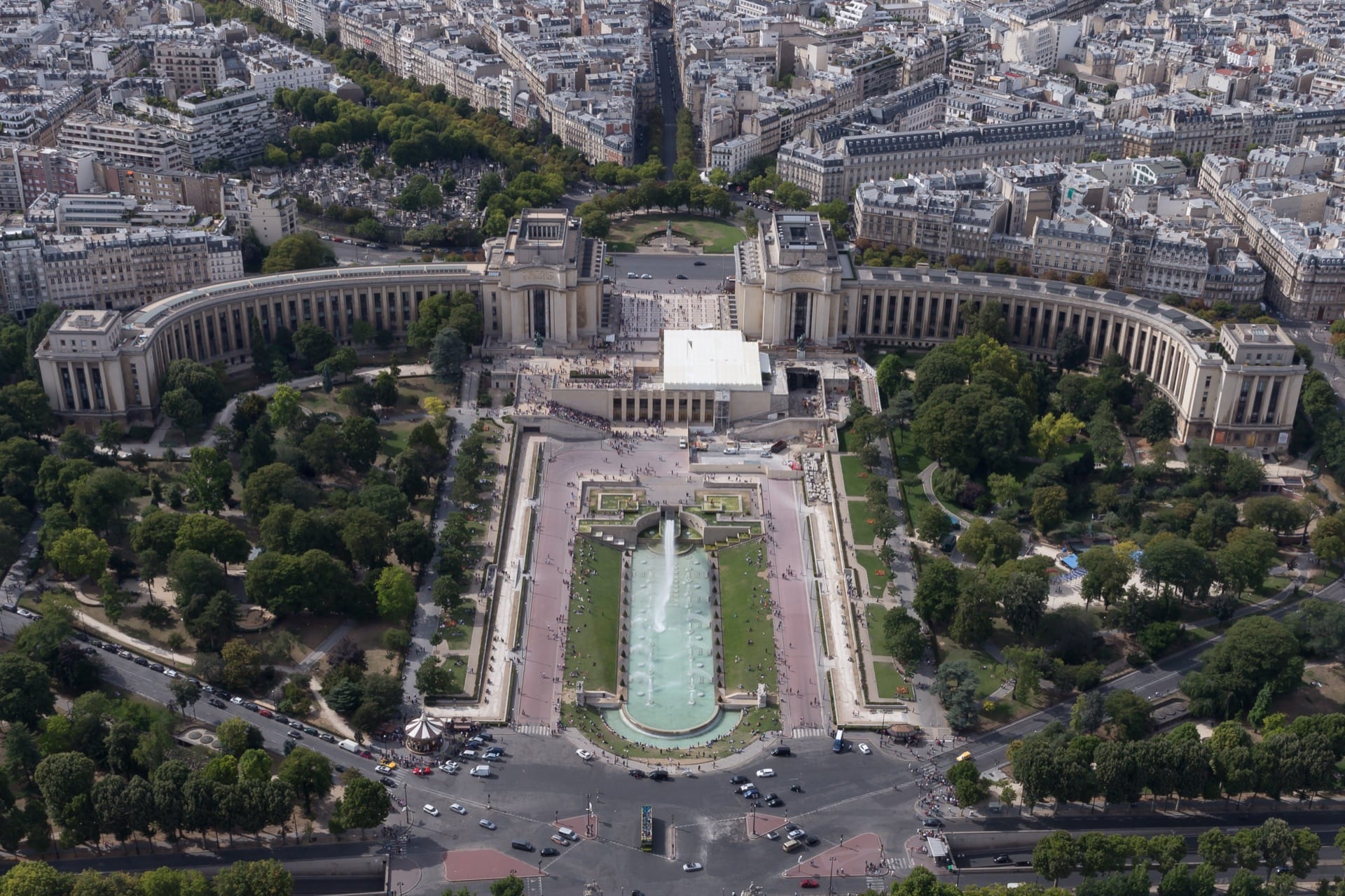 Vue aérienne du palais de Chaillot au Trocadéro : deux ailes courbes encadrant l’esplanade et les jardins à fontaines, Paris s’étendant à l’arrière-plan