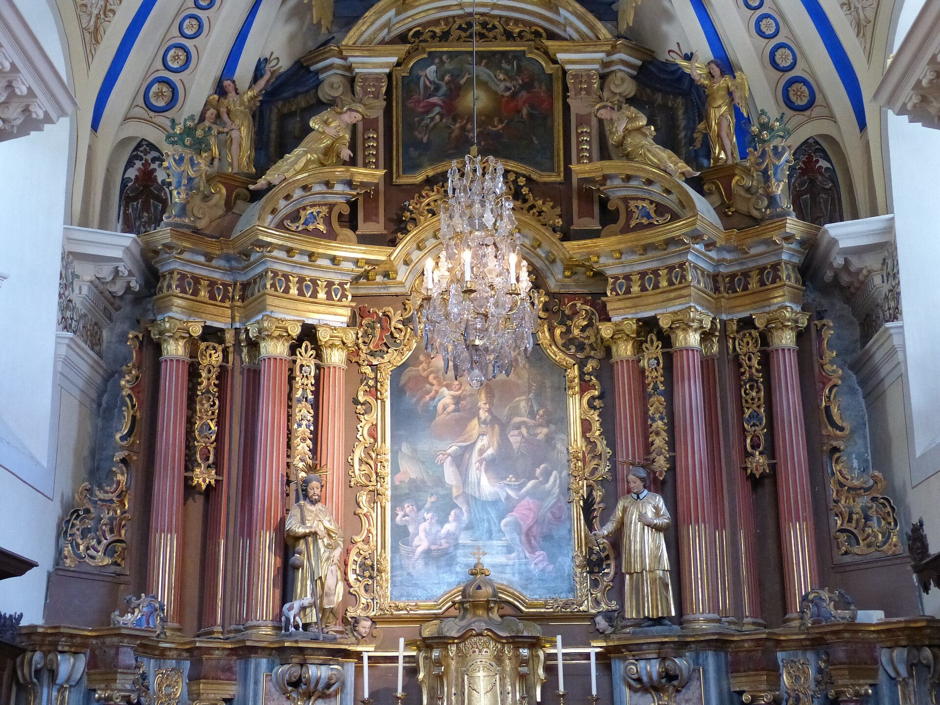 Retable baroque doré de l’église Saint-Nicolas-de-Véroce : colonnes torses rouges, statues dorées, tableau central et lustre de cristal