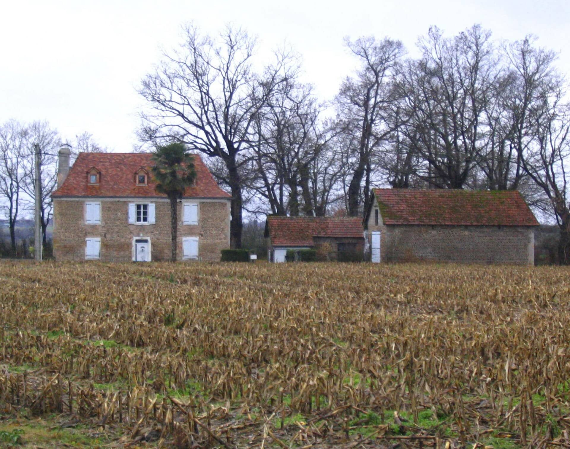 Maison de maître béarnaise en pierre à toit d’ardoise à croupes, devant un champ, à Auriac