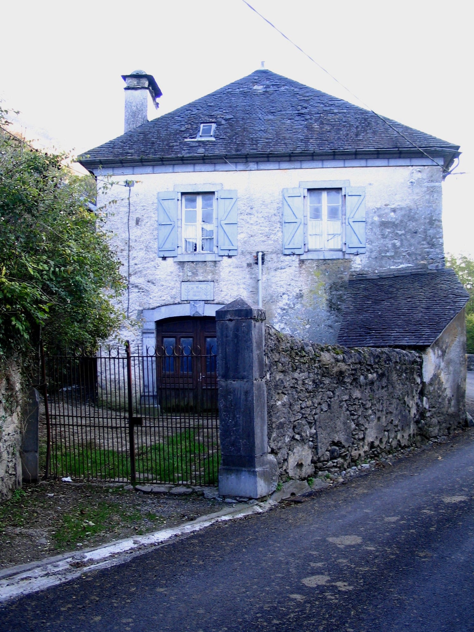Maison béarnaise en pierre à haut toit d’ardoise et portail charretier bleu, à Béon