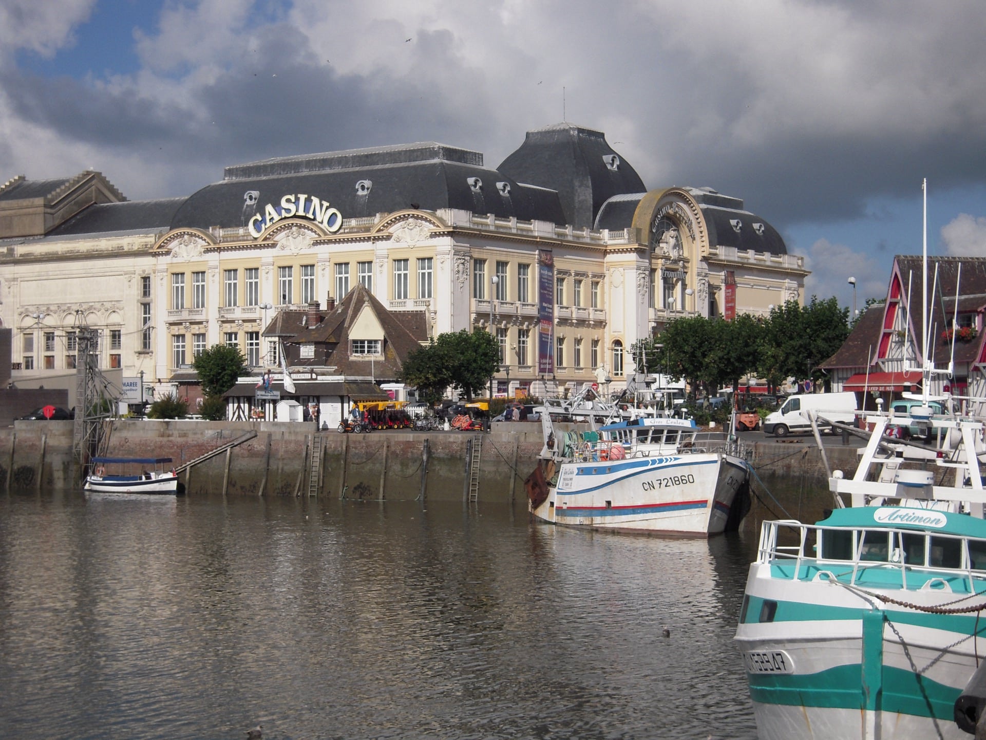 Le casino de Trouville, façade Belle Époque à dôme d’ardoise portant l’enseigne « Casino », vu depuis le port aux bateaux de pêche