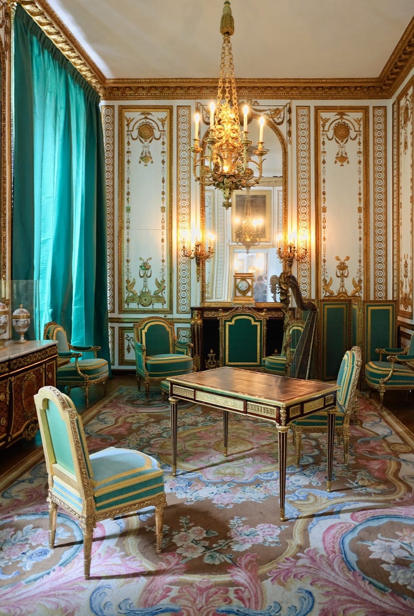 Angle du cabinet doré de Marie-Antoinette à Versailles : boiseries néoclassiques entièrement dorées, panneaux ornés de sphinx, de trépieds et de figures antiques sur fond blanc.