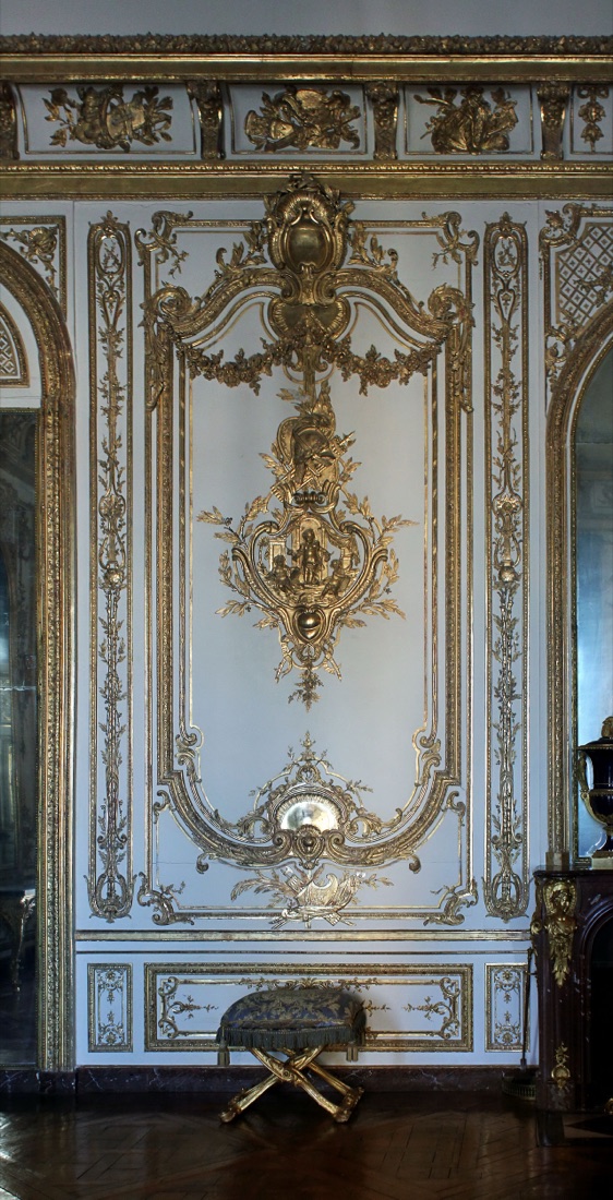 Détail d’un lambris rocaille du cabinet du Conseil à Versailles : coquilles, agrafes et rinceaux dorés asymétriques sculptés en relief sur un fond clair.