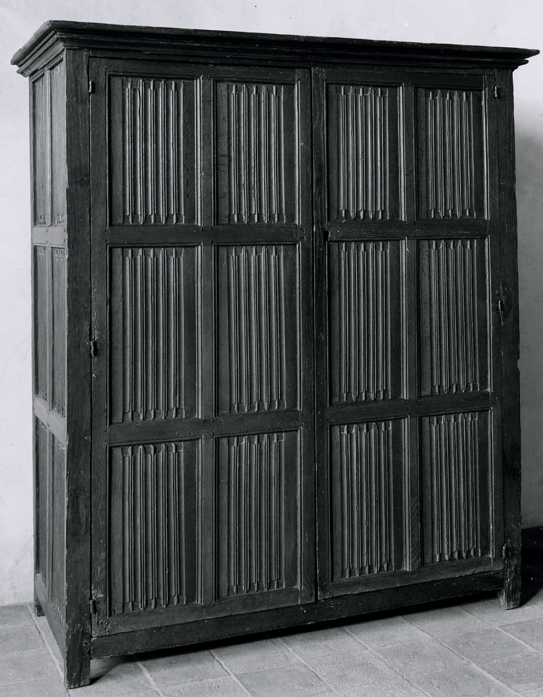 Meuble de rangement en chêne dont les vantaux sont sculptés de panneaux à plis-de-serviette, le bois imitant une étoffe verticalement repliée.