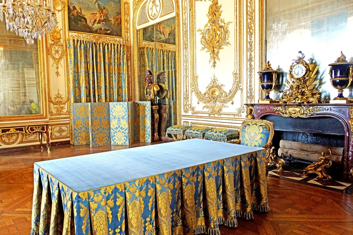 Vue large du cabinet du Conseil à Versailles : les murs sont couverts de boiseries de hauteur, panneaux moulurés courant de la plinthe à la corniche et rythmés d’ornements dorés.