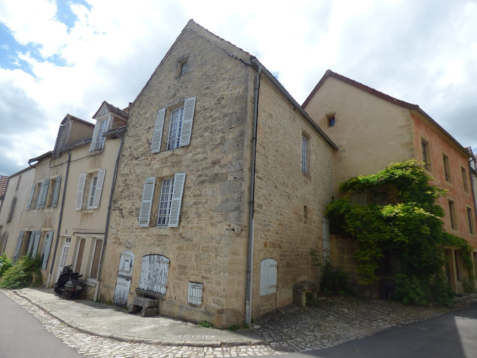 Angle de rue à Flavigny-sur-Ozerain : maisons de pierre de taille aux volets clairs, portes de cave, chaussée pavée