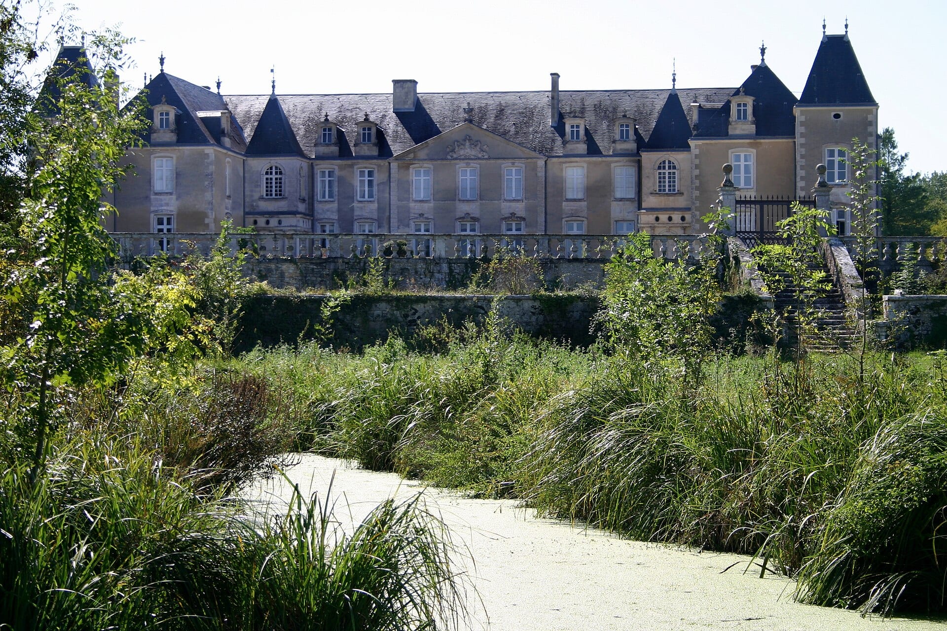 Le logis de Panloy, longue demeure classique à toits d’ardoise et tours, derrière des roseaux