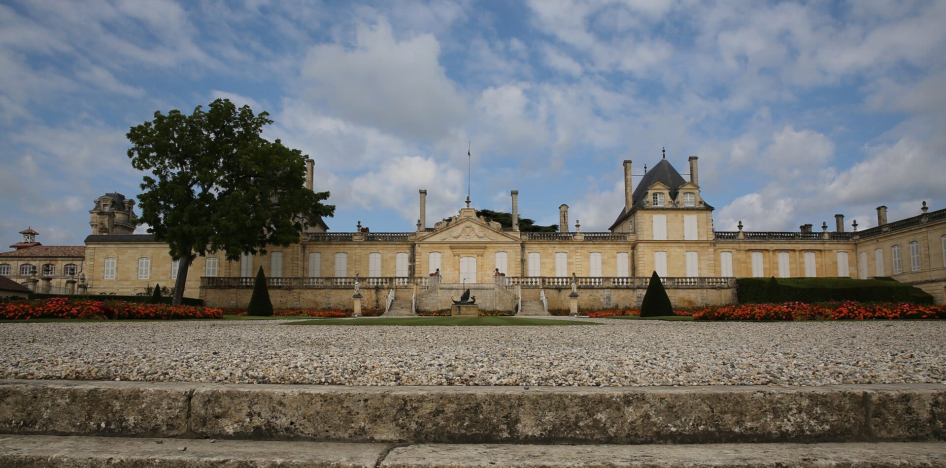 Longue façade basse blanche du château Beychevelle devant des jardins à la française