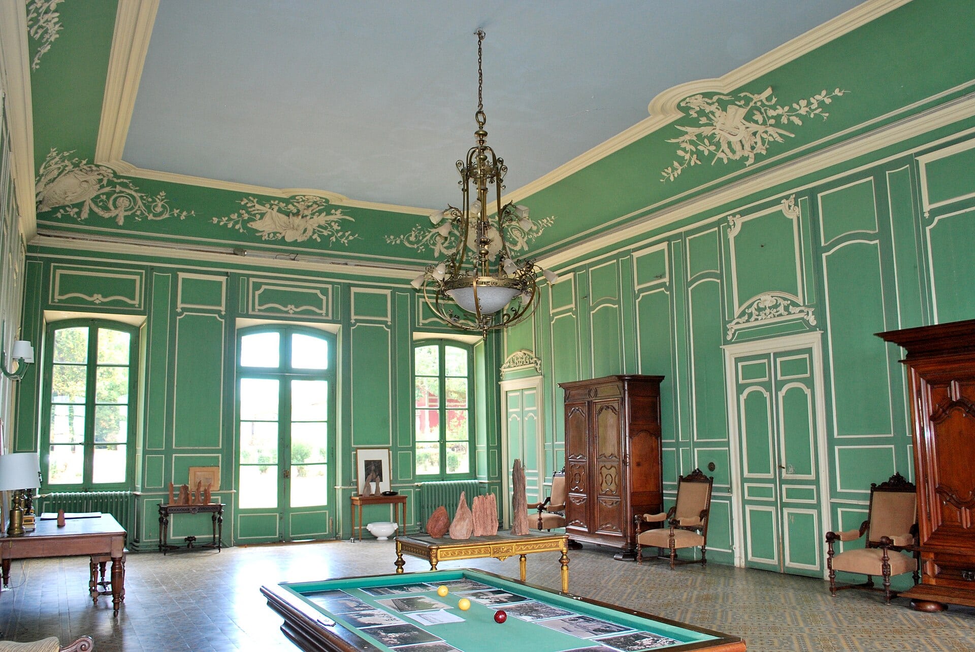 Salon aux boiseries vertes et lustre, avec table de billard, au domaine de Sybirol