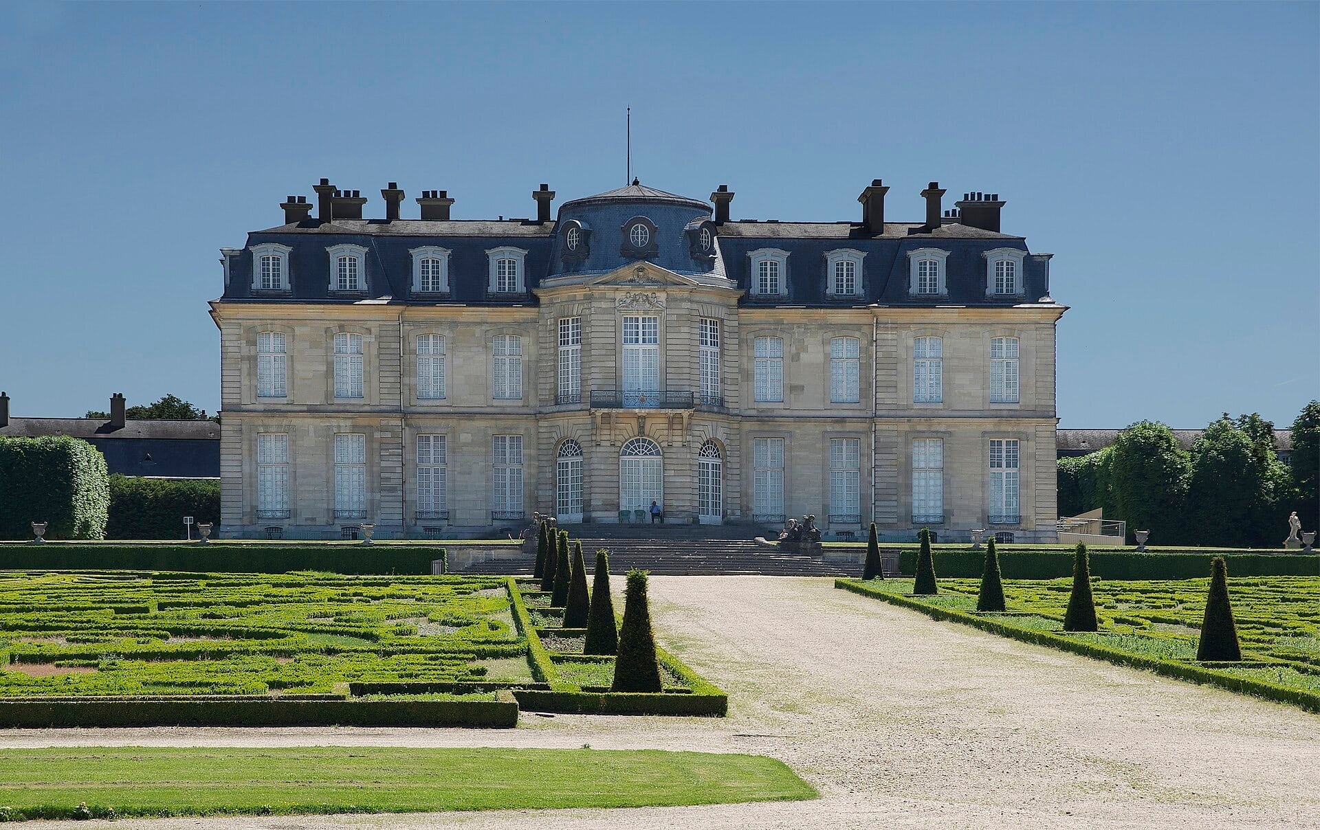 Façade sur jardin du château de Champs-sur-Marne : corps de logis de pierre symétrique, avant-corps central arrondi à fronton et dôme surbaissé, comble d’ardoise à lucarnes, parterre de broderie au premier plan