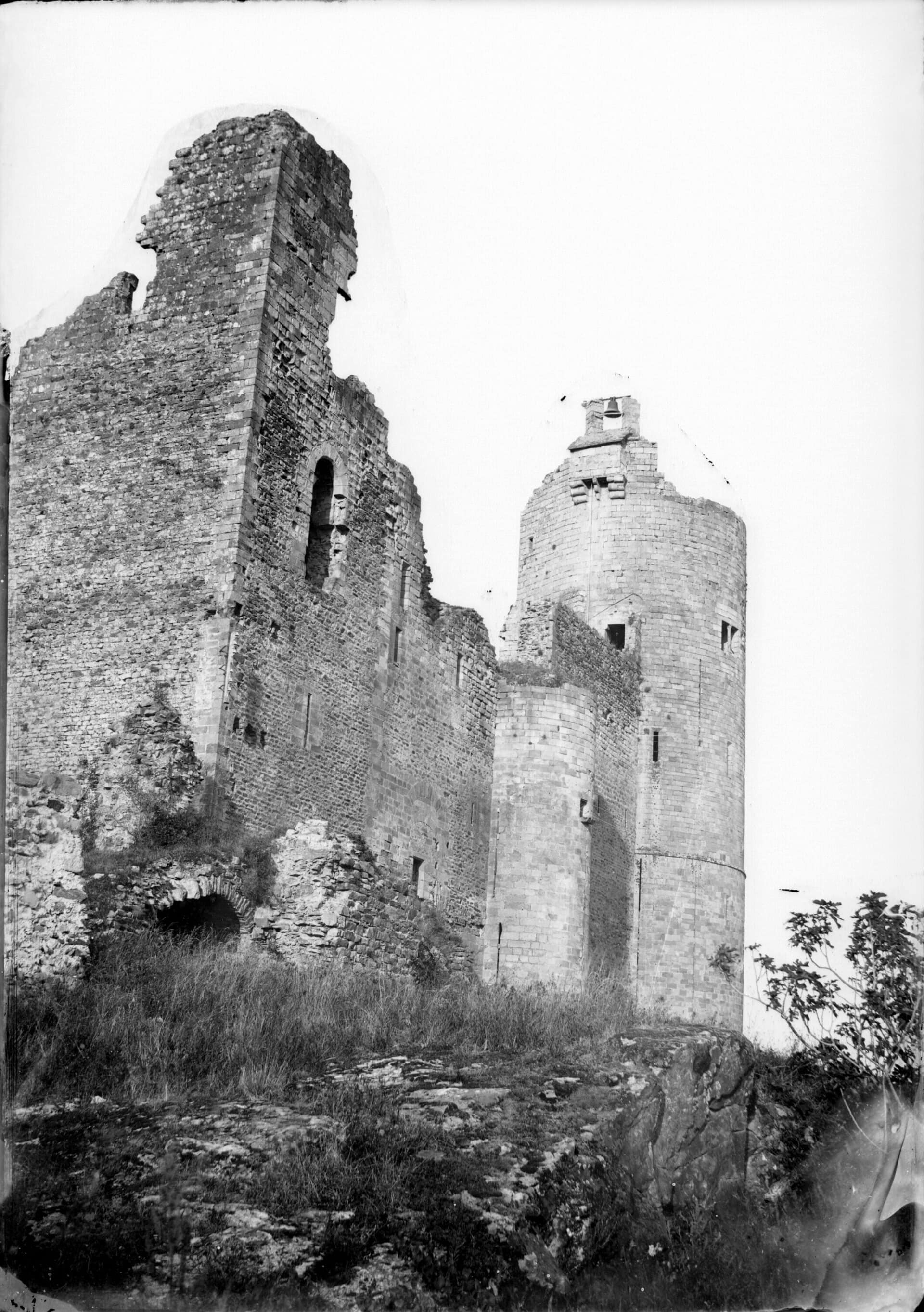 Photographie ancienne en noir et blanc : le donjon circulaire de Najac et un pan de logis ruiné percé de hautes et fines archères, sur un sommet rocheux