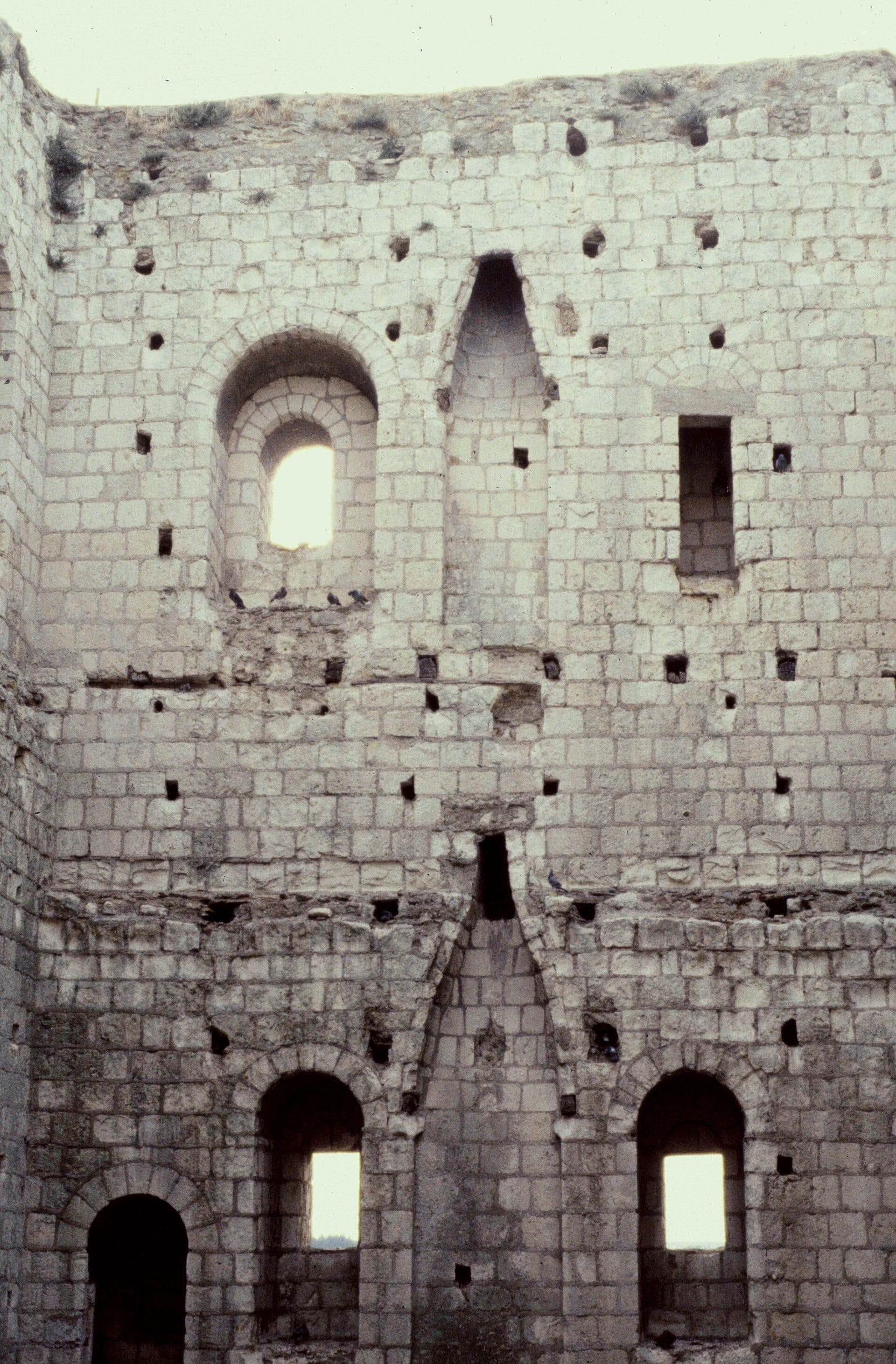 Intérieur du donjon roman de Loches à ciel ouvert : hauts murs de calcaire, baies en plein cintre, trous de boulin