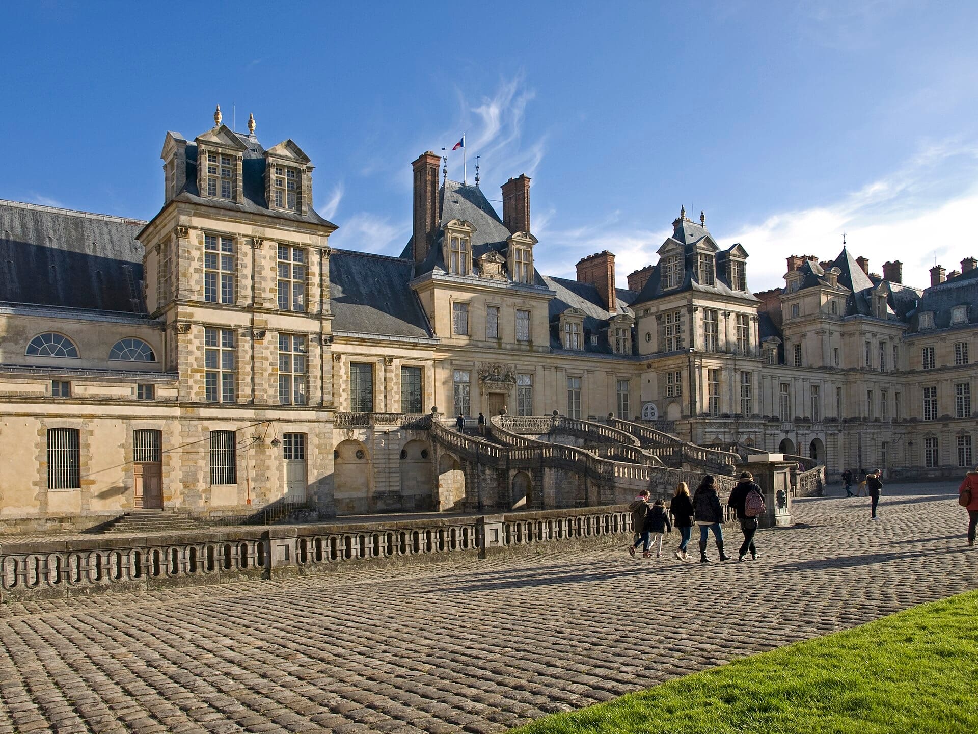 Cour du Cheval Blanc à Fontainebleau : escalier extérieur en fer-à-cheval à double volée courbe au centre, ailes de bâtiments à pavillons et hauts combles, sol pavé