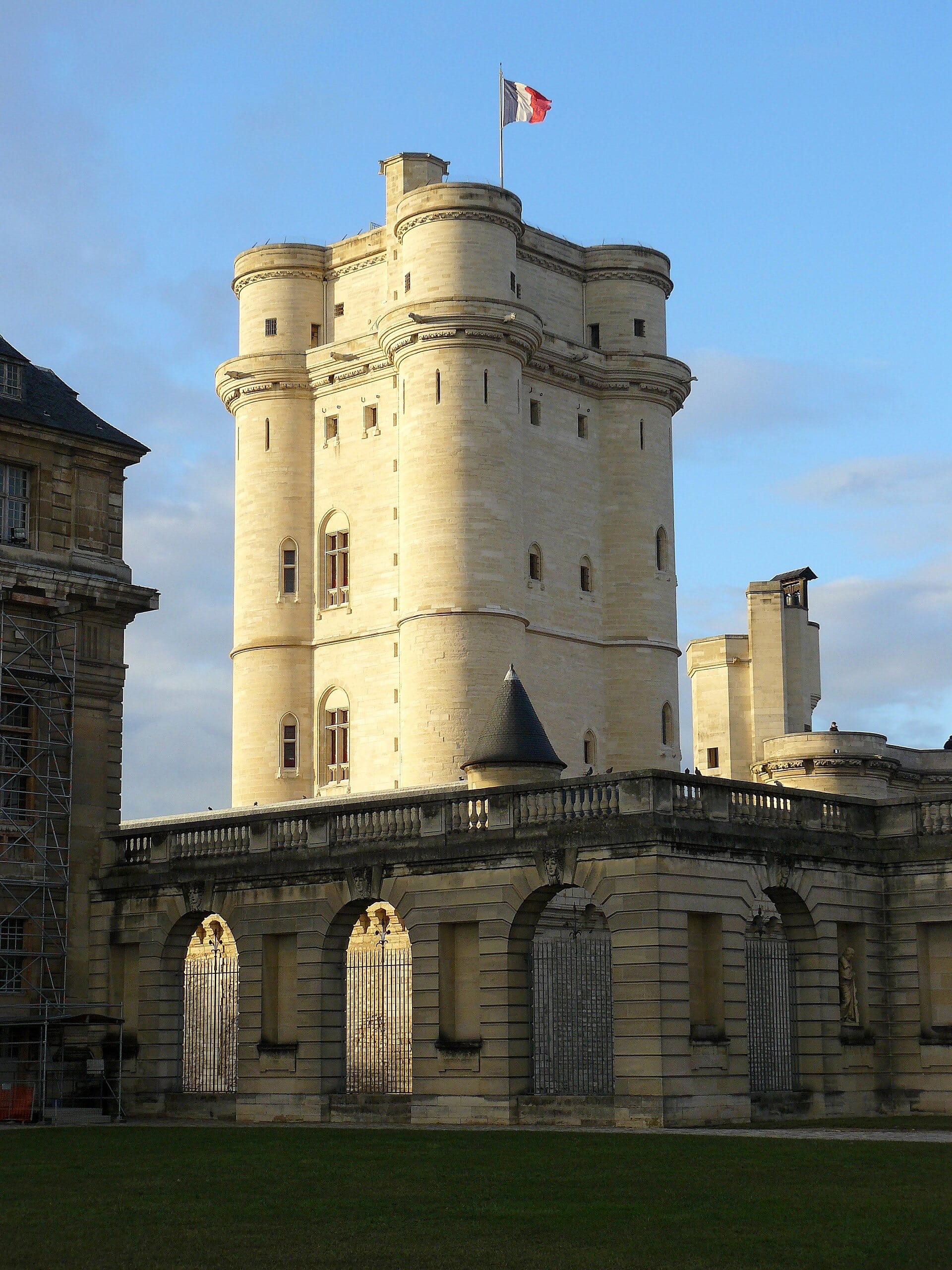 Le donjon du château de Vincennes, haute tour quadrangulaire à tourelles d’angle, drapeau au sommet, châtelet à arcades au premier plan