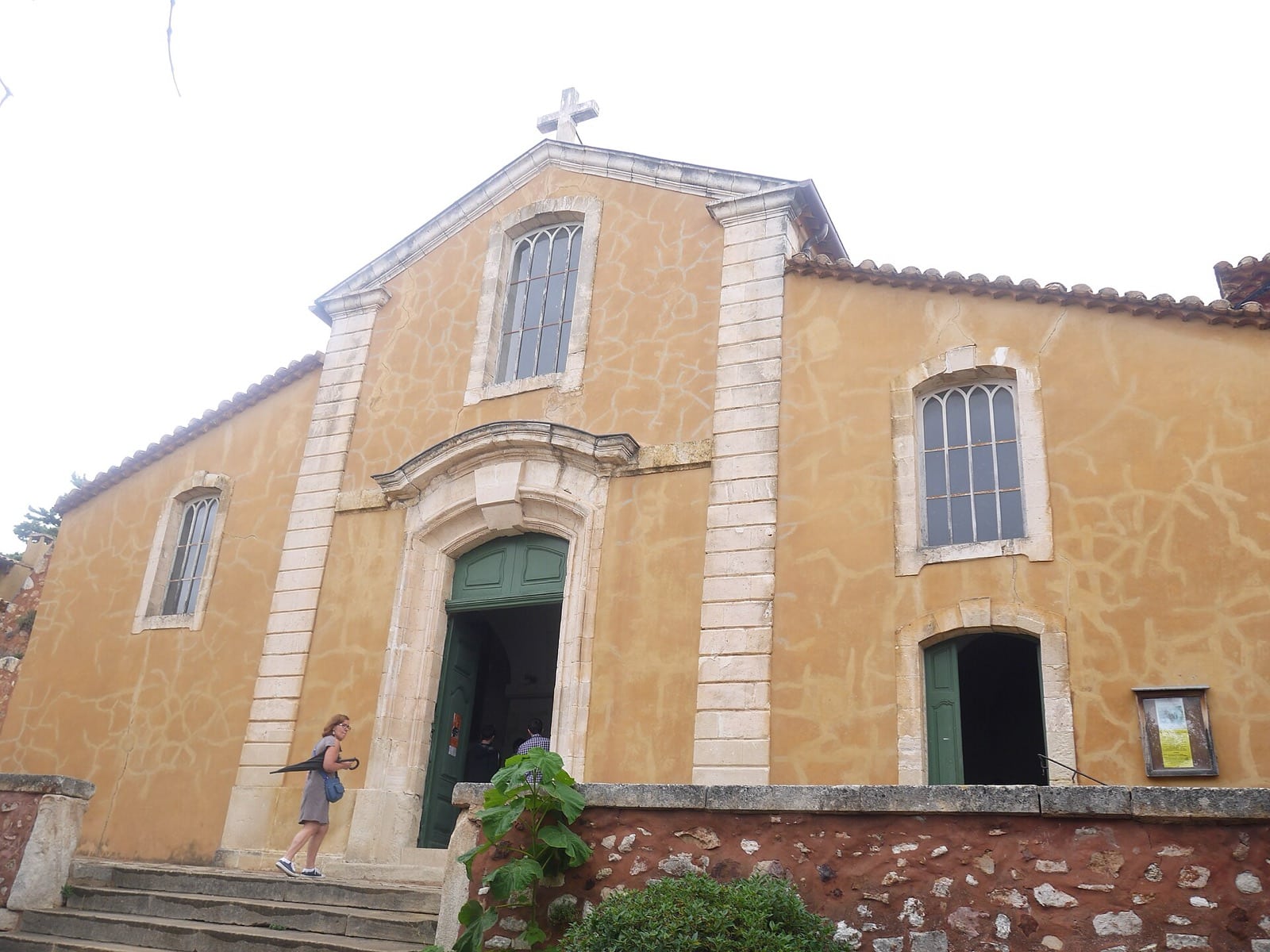 Façade d’église enduite d’un badigeon de chaux teinté d’ocre, aux fissures fines, à Roussillon