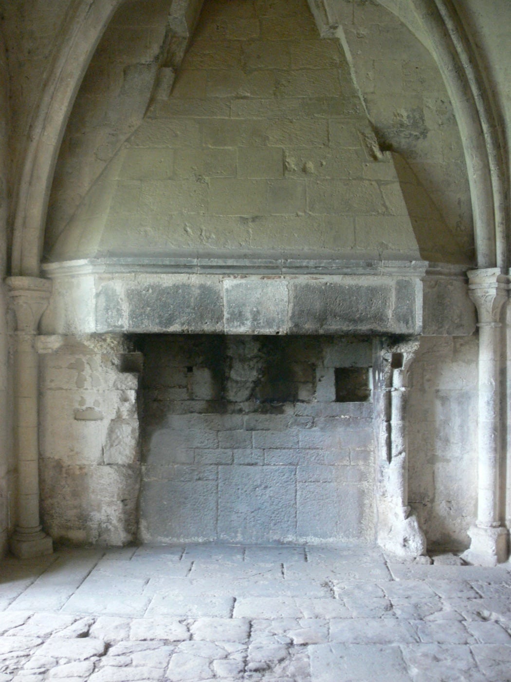 Grande cheminée médiévale en pierre à hotte saillante occupant un pan de mur, dans la salle des moines de l’abbaye de Silvacane.