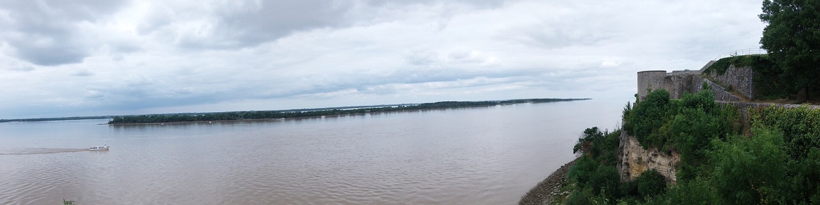 Vue panoramique de l’estuaire de la Gironde, large étendue d’eau sous un ciel nuageux ; à l’extrémité droite, un rempart de pierre et une tour de la citadelle de Blaye couronnent une falaise boisée.