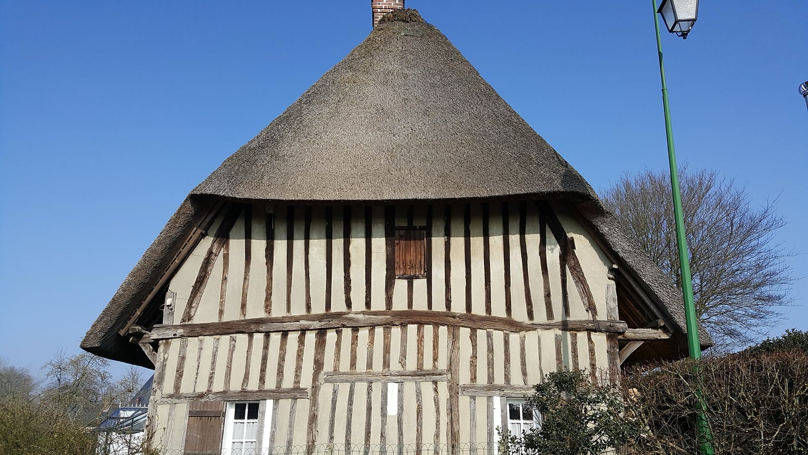 Chaumière normande à colombage, poteaux de bois verticaux serrés et toit de chaume