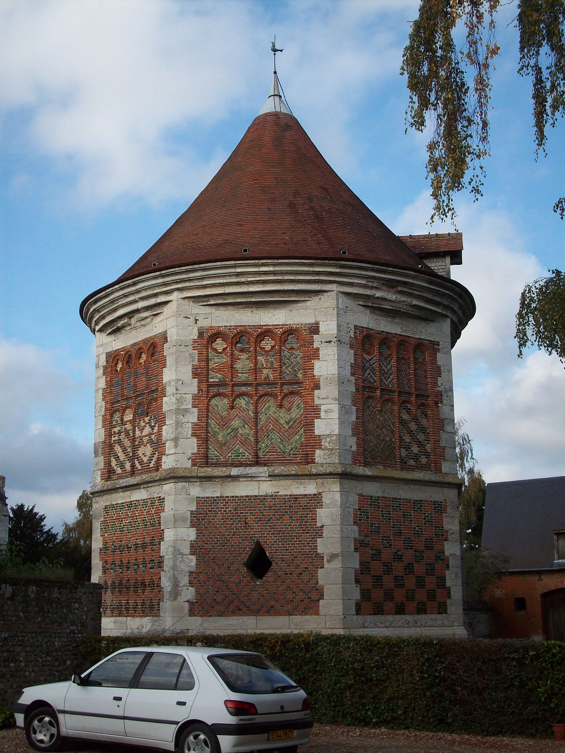 Le colombier Renaissance de Boos (Seine-Maritime), tour octogonale à toit conique, aux façades en damier de brique rouge, de brique vernissée et de pierre.