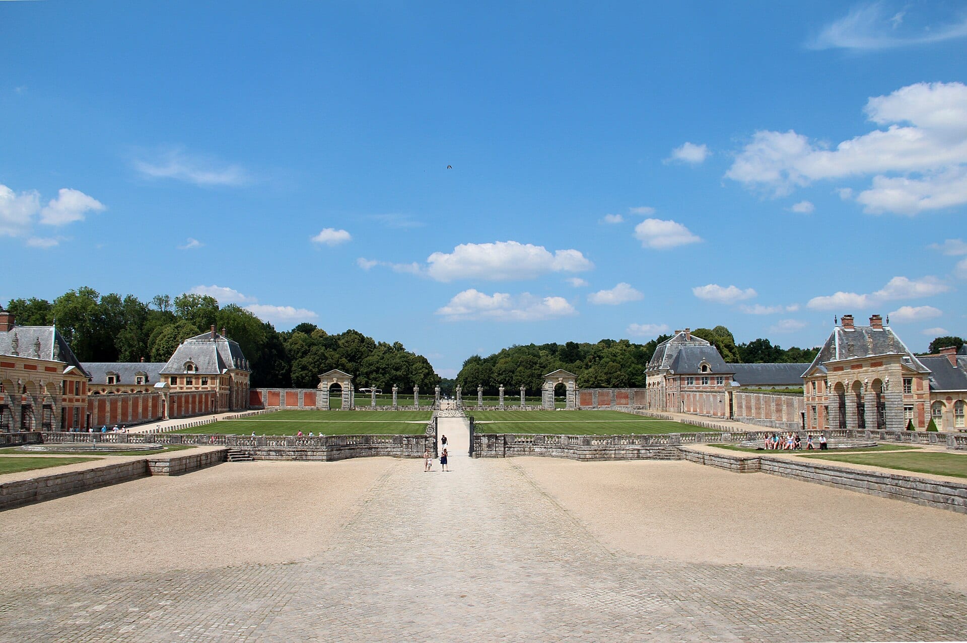 Les deux ailes de communs en brique et pierre encadrant l’avant-cour de Vaux-le-Vicomte, grilles et perspective vers le parc.