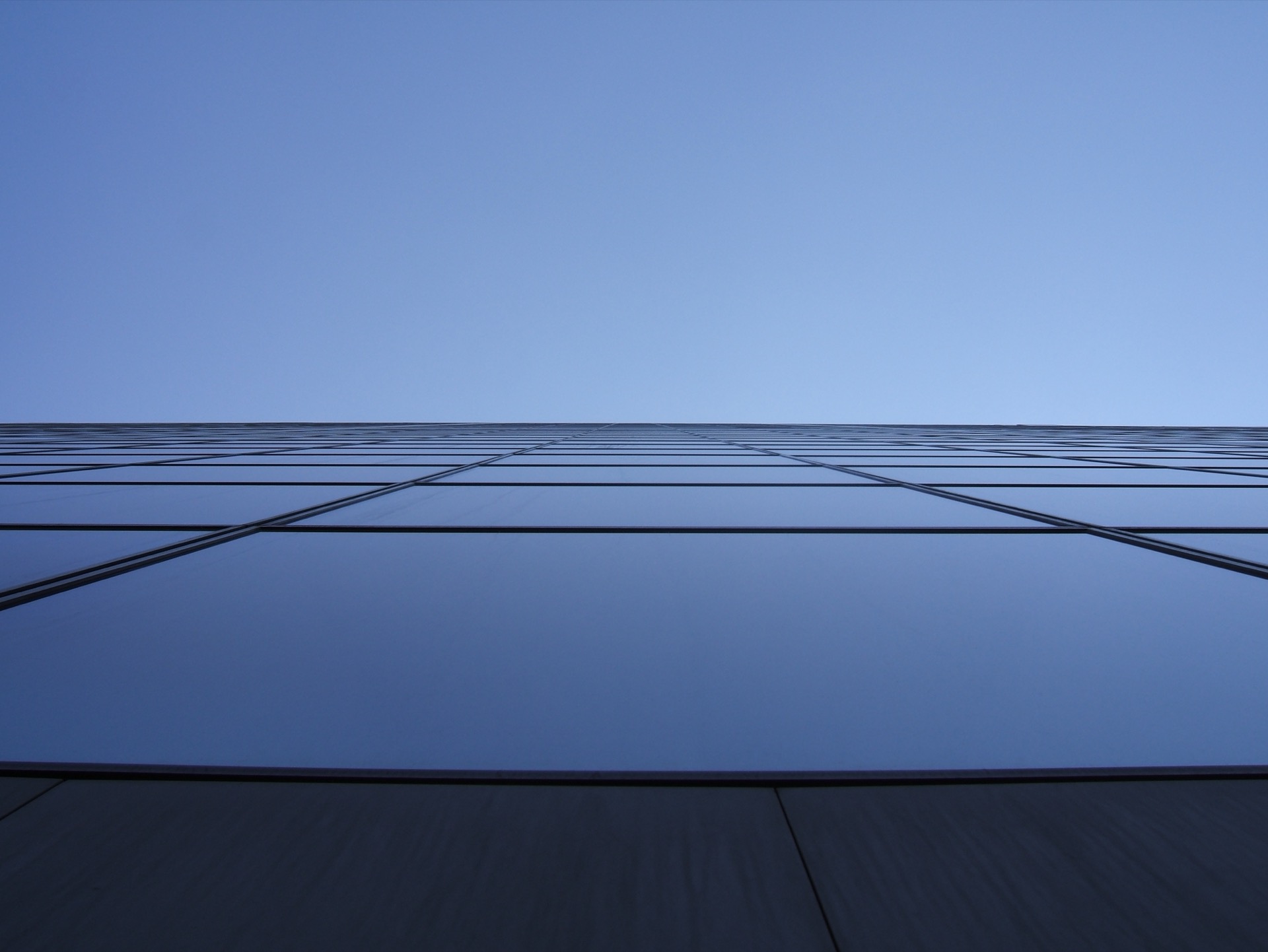 En contre-plongée, le vaste mur-rideau de verre quadrillé de la Grande Arche de la Défense se découpant sur un ciel bleu