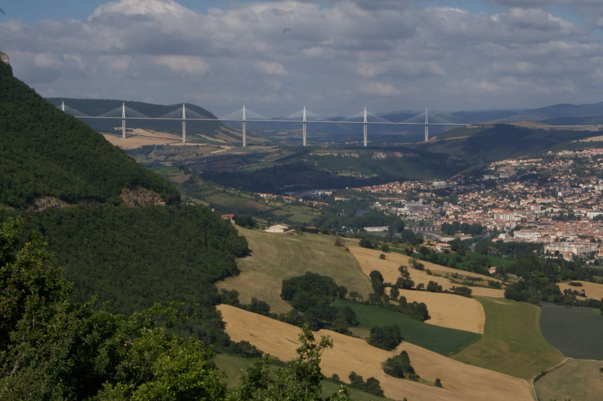 Le viaduc de Millau, pont à haubans aux hauts pylônes blancs franchissant la vallée du Tarn, la ville de Millau et les collines en contrebas