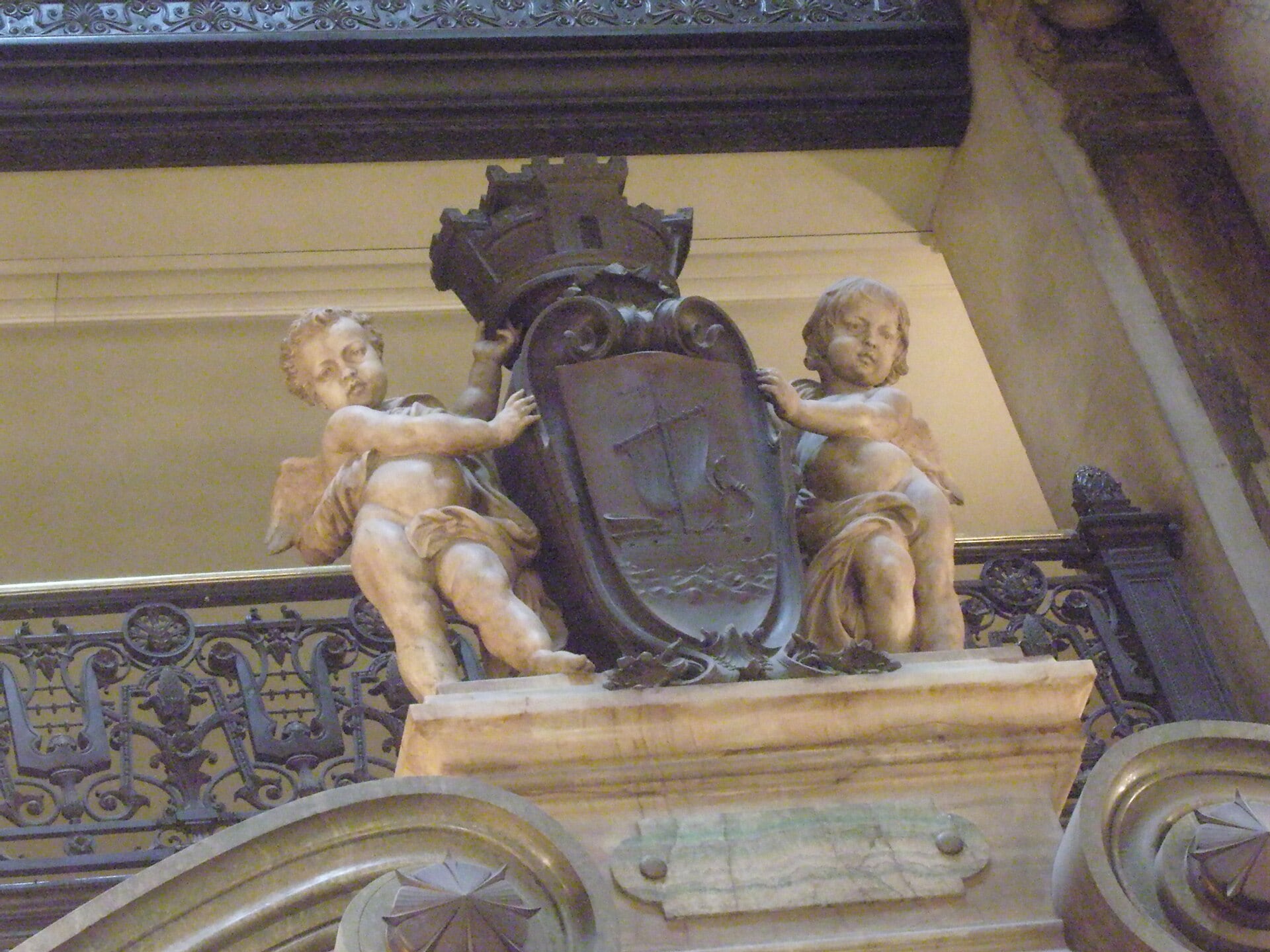 Détail du grand escalier de l’Opéra Garnier : les armoiries de la Ville de Paris, au navire, portées par deux putti, au-dessus d’un palier de marbre.