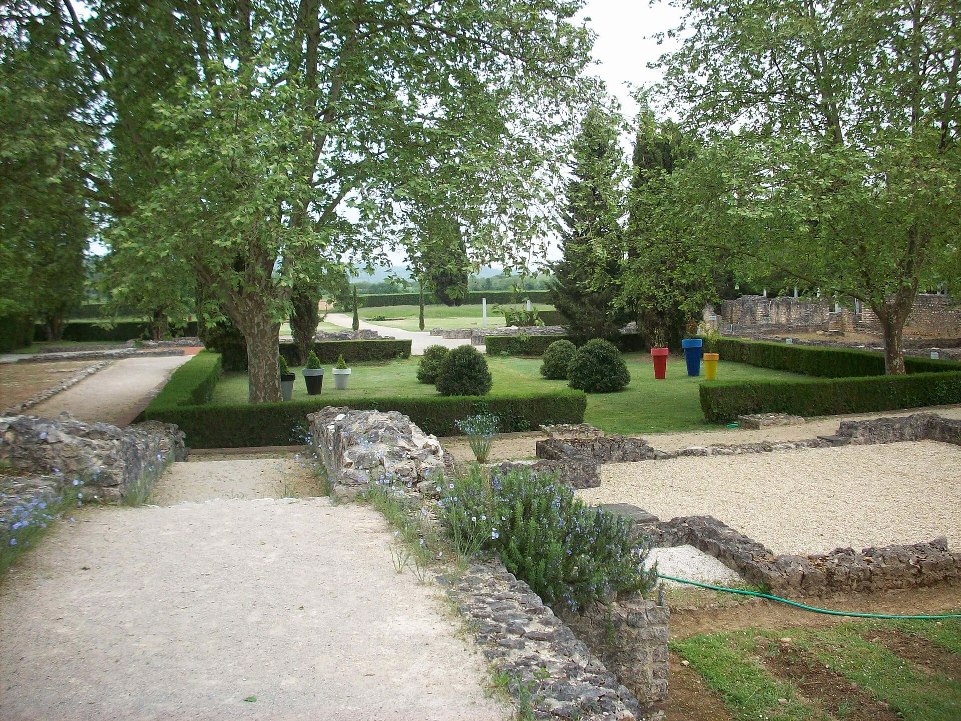 Vestiges arasés de la villa gallo-romaine de Montmaurin : fondations de murs au ras du sol dessinant les pièces, allées de gravier et jardin d’agrément aménagé entre les arbres