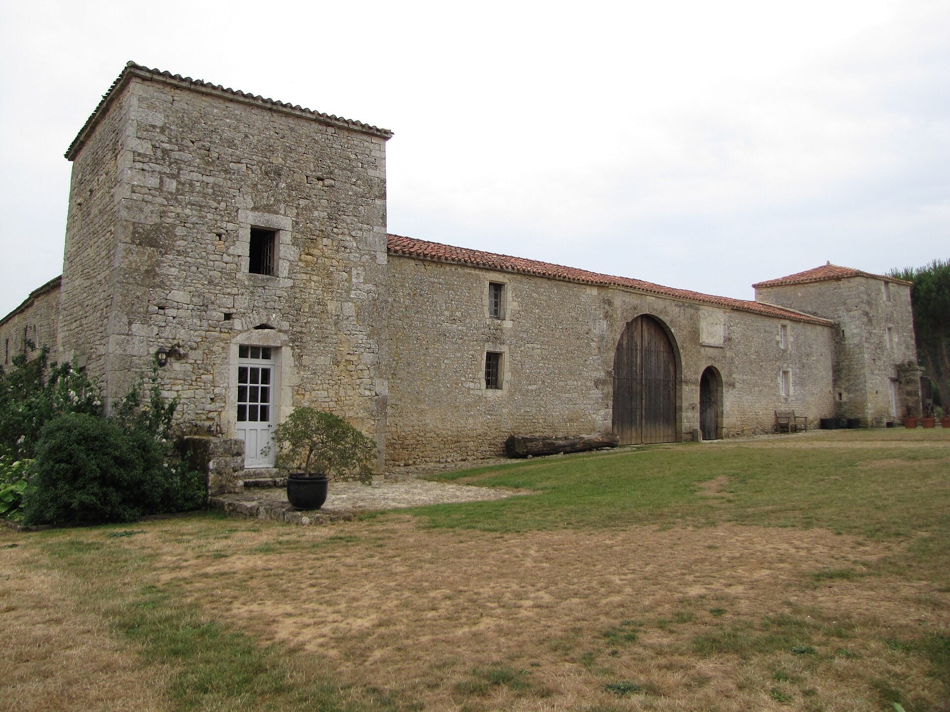 Petit logis noble de pierre calcaire : tour-pavillon carrée coiffée de tuiles, longue aile basse percée d’une grande porte charretière en plein cintre, sur une pelouse