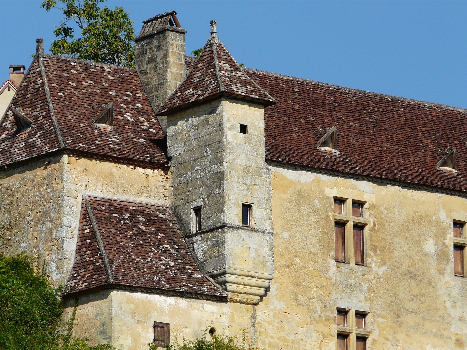 Détail d’un logis périgourdin : tourelle d’escalier en encorbellement sur cul-de-lampe, coiffée d’un toit conique de tuiles, fenêtres à croisée de pierre et lucarnes à fronton