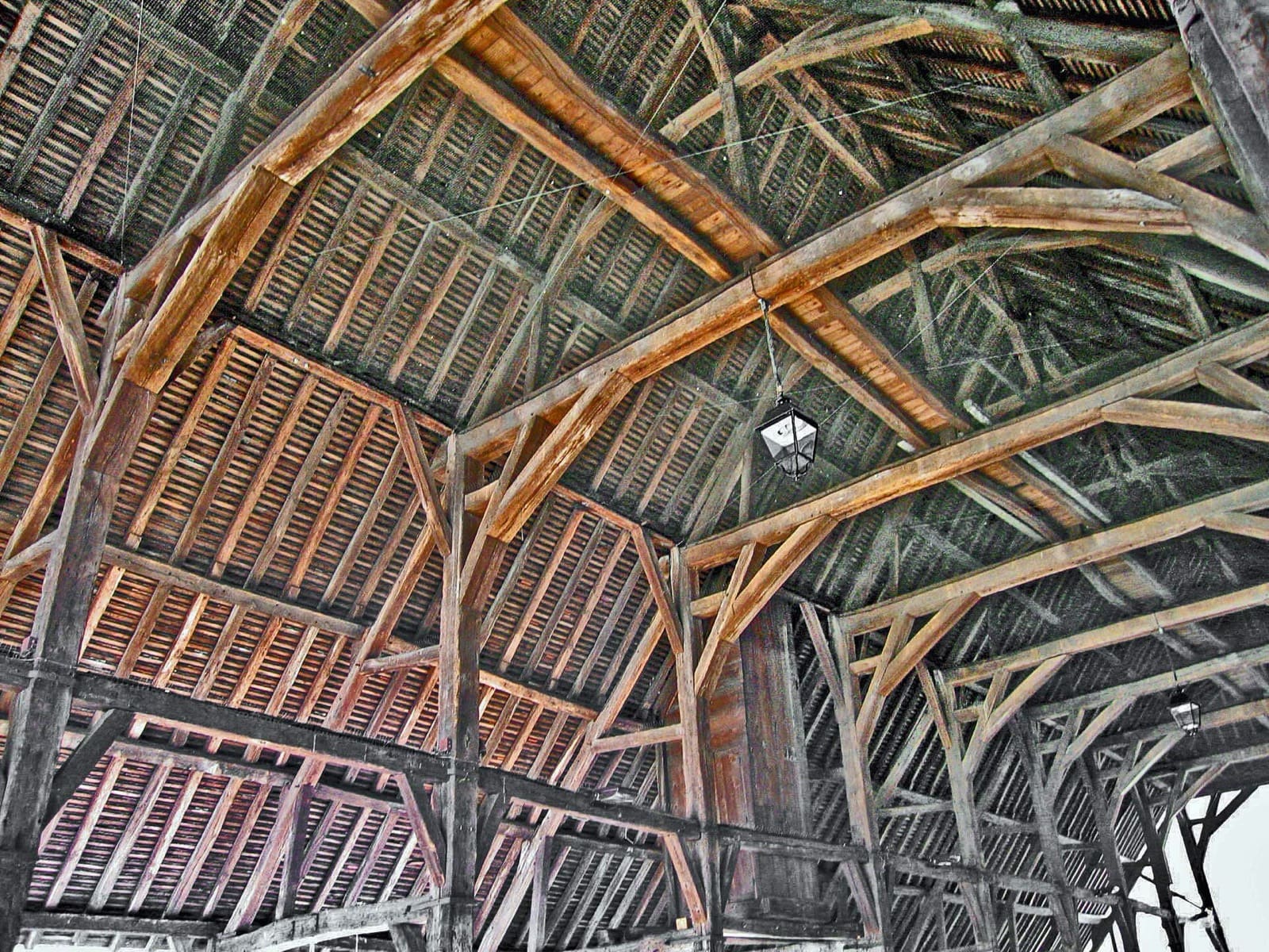 Charpente de bois vue de dessous à l’intérieur de la halle d’Arpajon : poteaux, entraits et assemblages de la structure