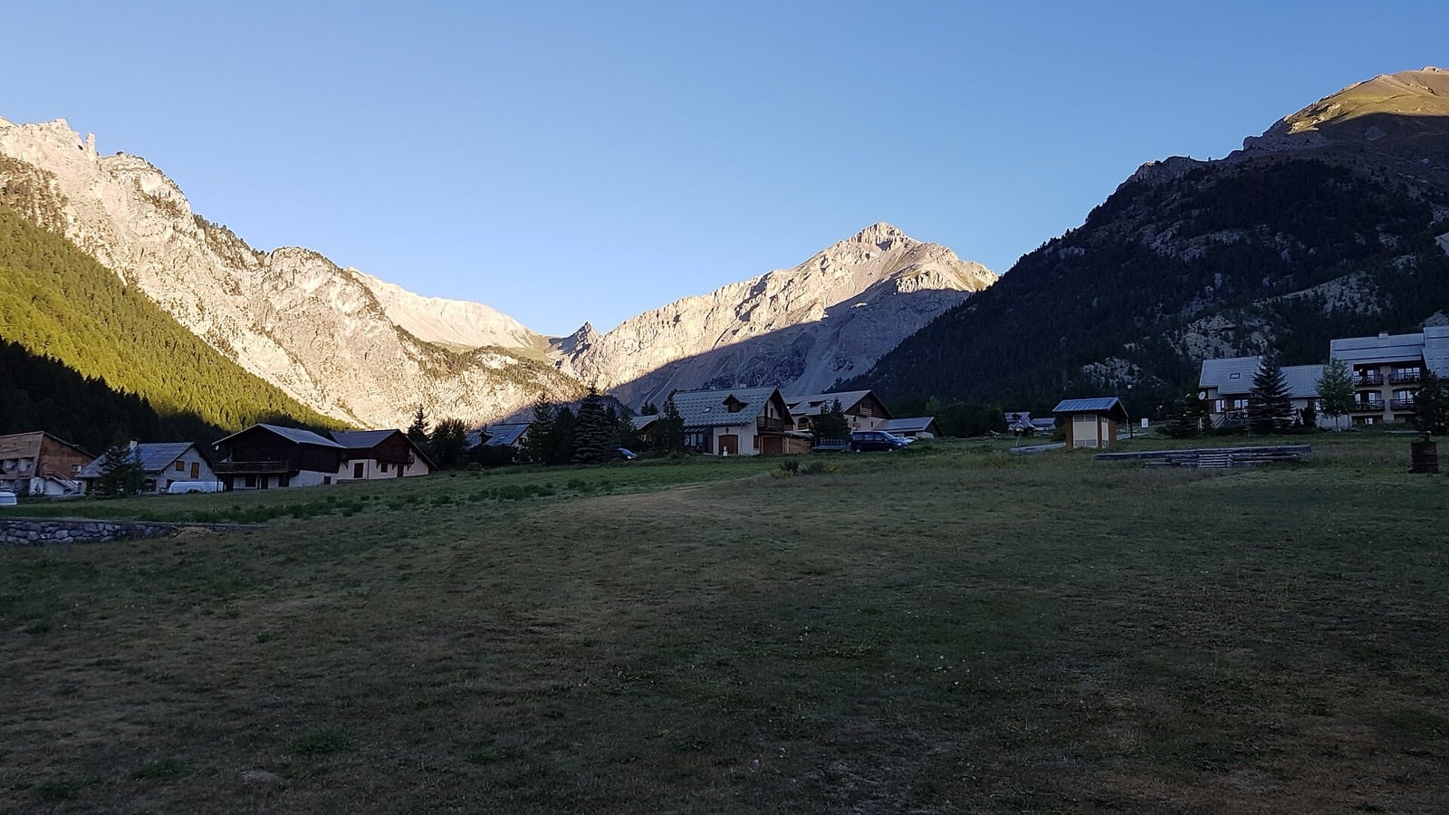 Chalets de pierre et de bois groupés à flanc de vallée à Brunissard, dans le Queyras, sous une lumière rasante