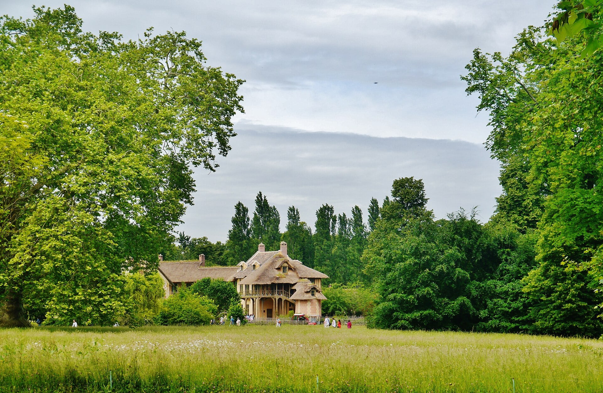 Le Hameau de la Reine à Versailles : chaumières à pans de bois et toits de chaume au bord d’un pré.
