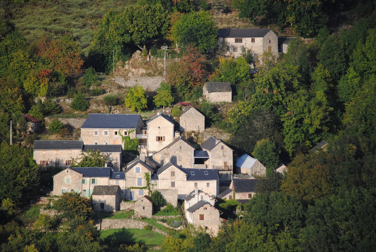 Une dizaine de maisons de pierre à toits de schiste serrées à flanc de coteau cévenol, au Mourier, en automne