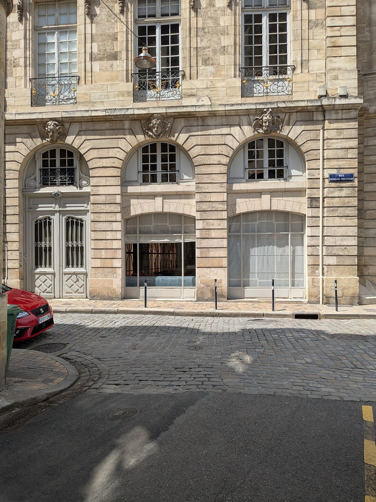 Façade d’hôtel particulier bordelais : mascarons sculptés (masques de faune et de femme) au-dessus des baies cintrées, balcons de ferronnerie à l’étage