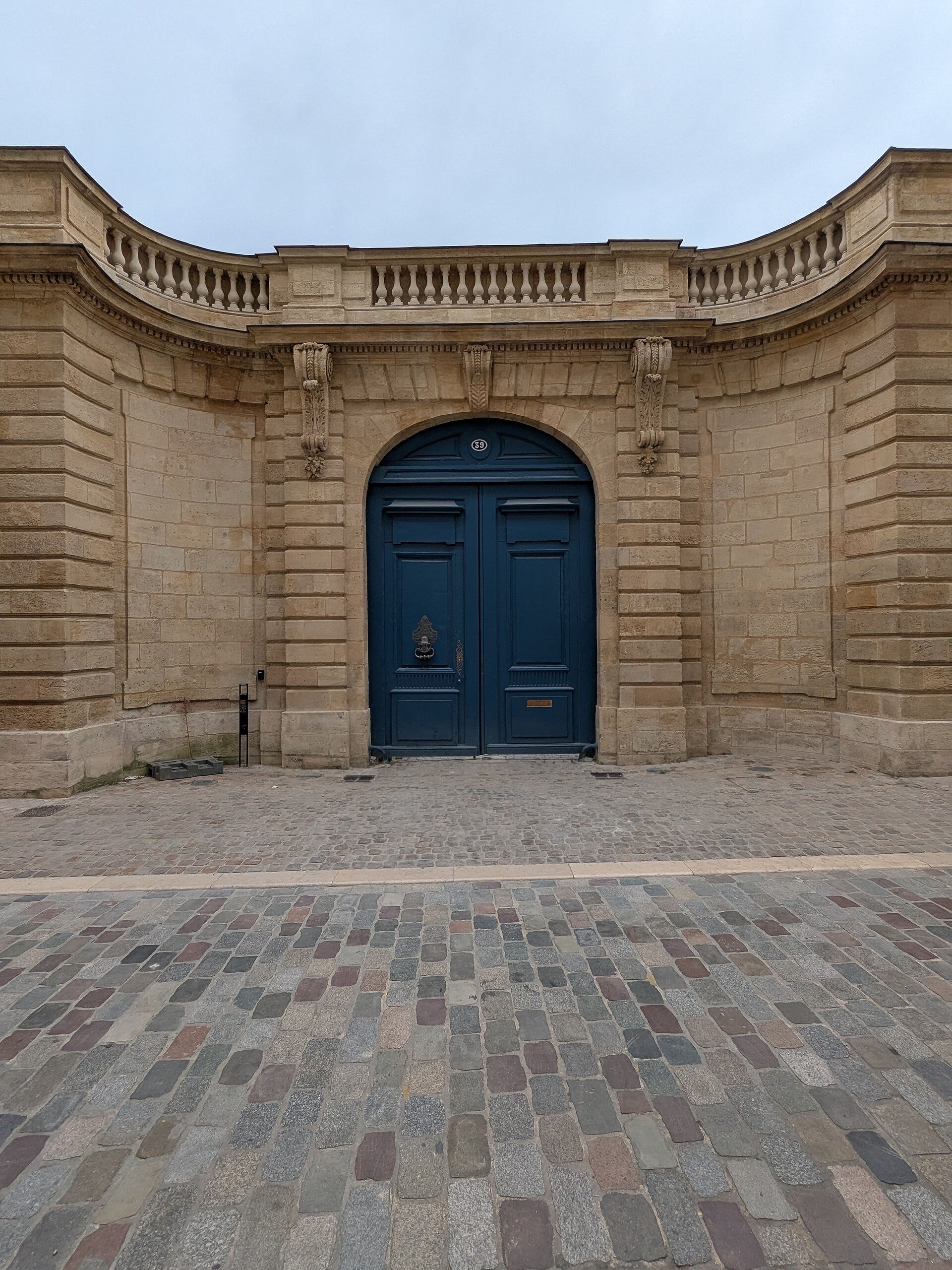 Porte cochère d’hôtel particulier : grand portail en plein cintre à deux vantaux, encadrement de pierre à bossage et balustrade, sur une cour pavée