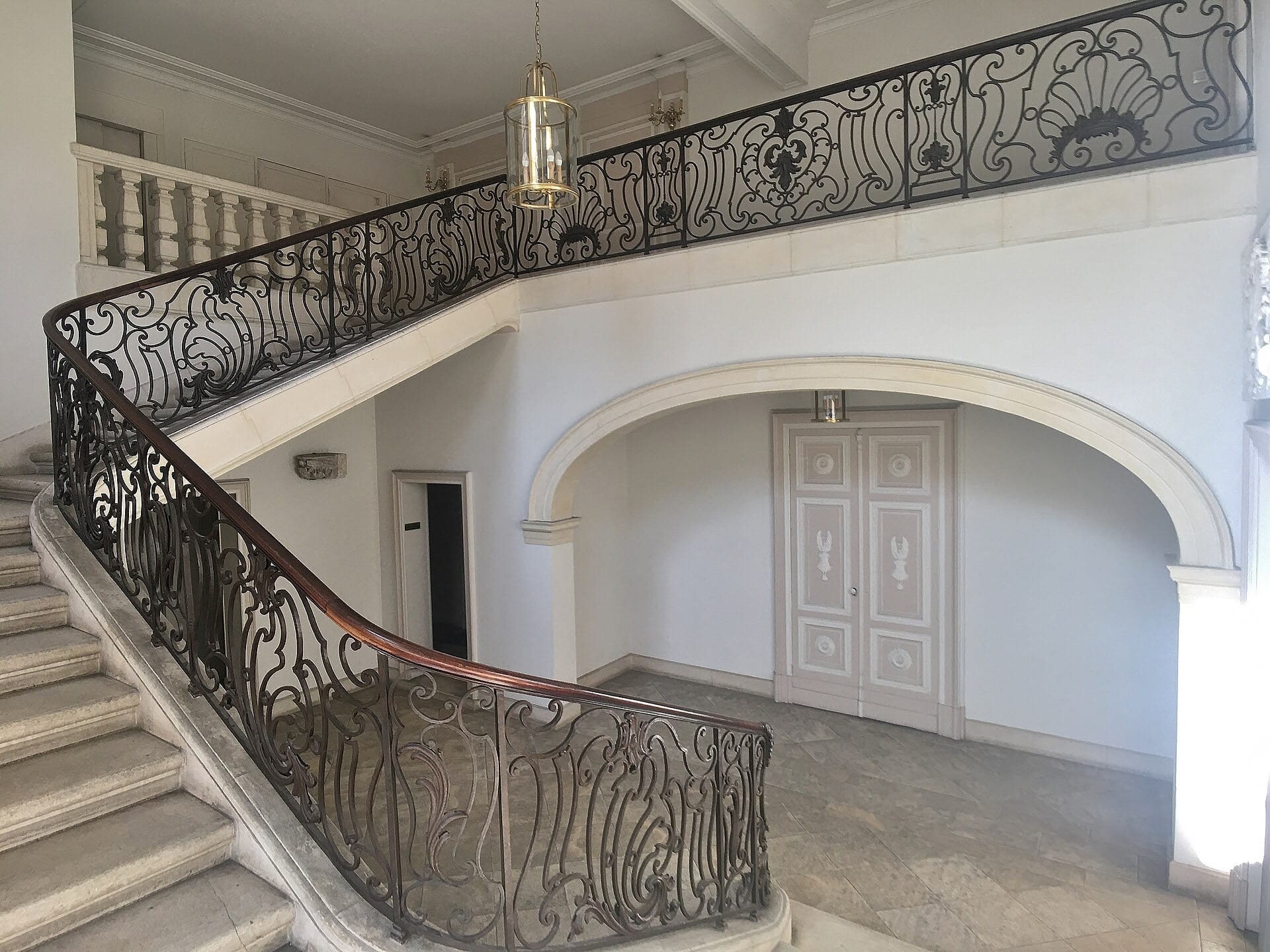 Escalier d’honneur d’hôtel particulier : marches de pierre, rampe de fer forgé à volutes et rocailles, arcade et lanterne suspendue