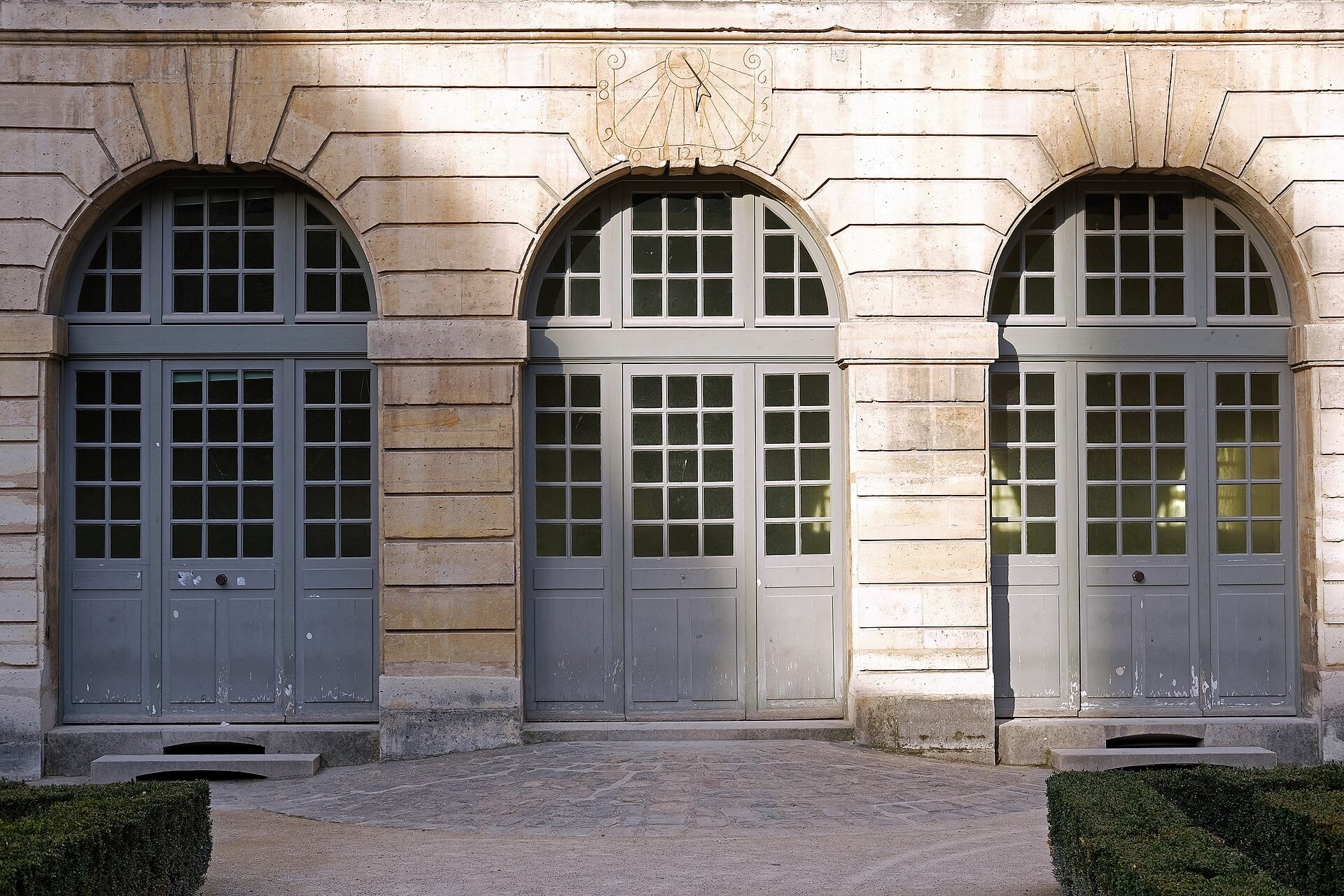 Façade sur jardin de l’hôtel de Sully : trois arcades en plein cintre, cadran solaire sculpté, parterres de buis taillés
