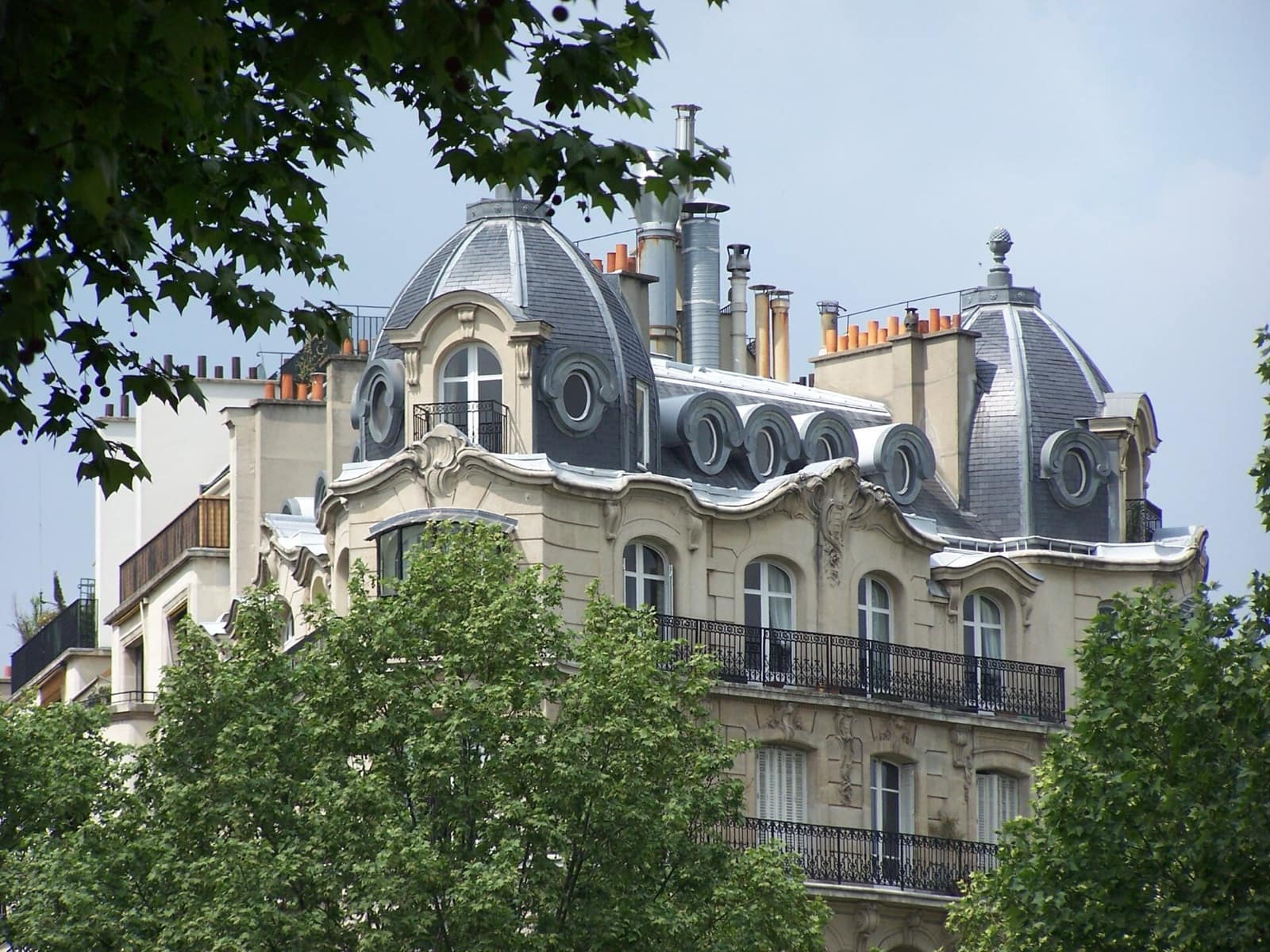 Couronnement d’un immeuble haussmannien : deux toits en dôme d’ardoise, comble brisé à lucarnes à œil-de-bœuf, souches de cheminées et étage attique sculpté