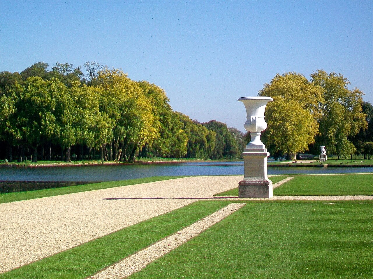 Le Grand Canal du parc de Chantilly, dessiné par Le Nôtre, bordé d’allées et de pelouses géométriques, un grand vase de pierre sur piédestal au premier plan.