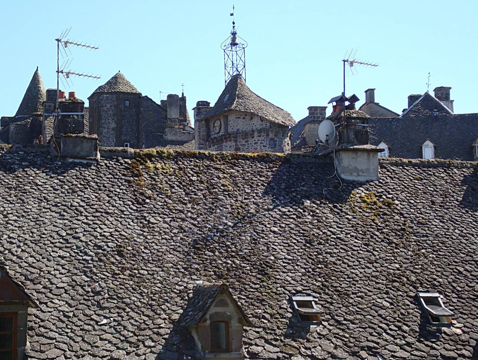 Toitures de lauze sombre du bourg de Salers, dans le Cantal, sous un clocheton de fer forgé