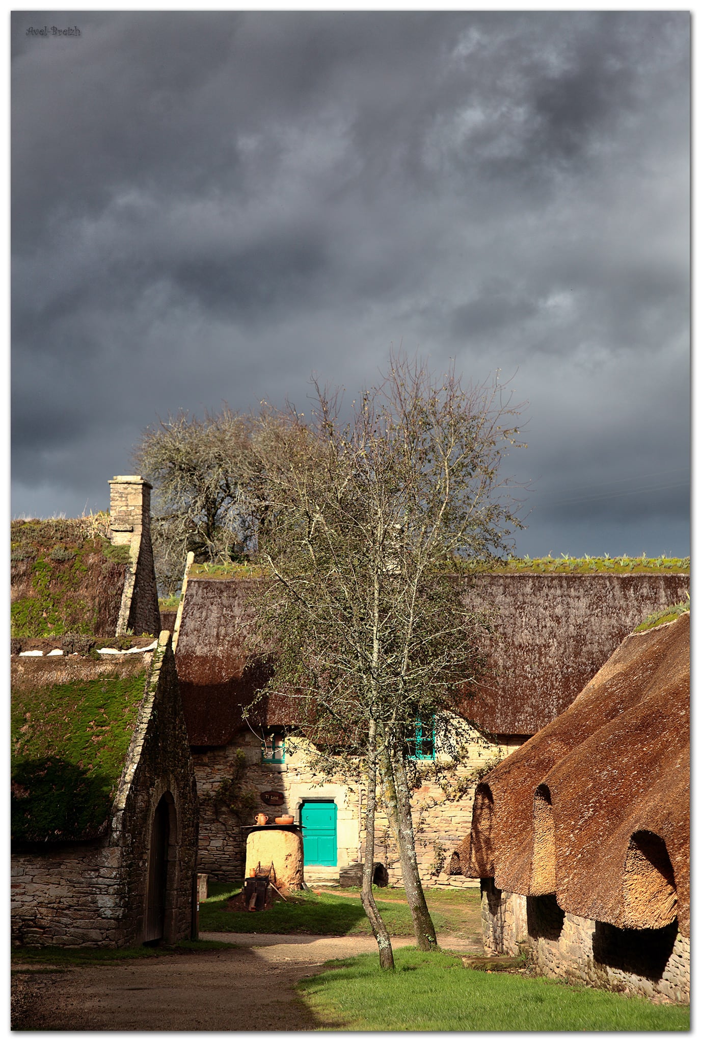 Hameau de longères bretonnes sous un ciel d’orage