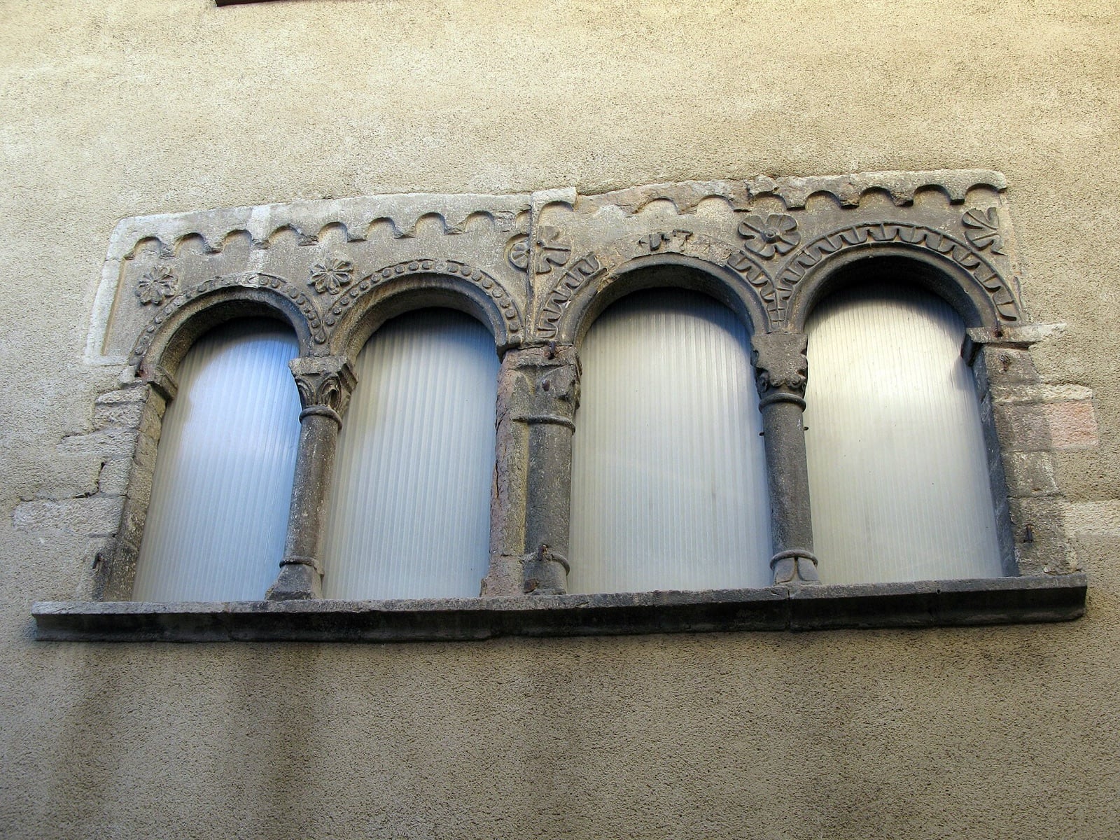 Baie romane en pierre percée de quatre arcs en plein cintre portés par des colonnettes à chapiteaux, ornée de rosaces sculptées, dans une façade de Cluny