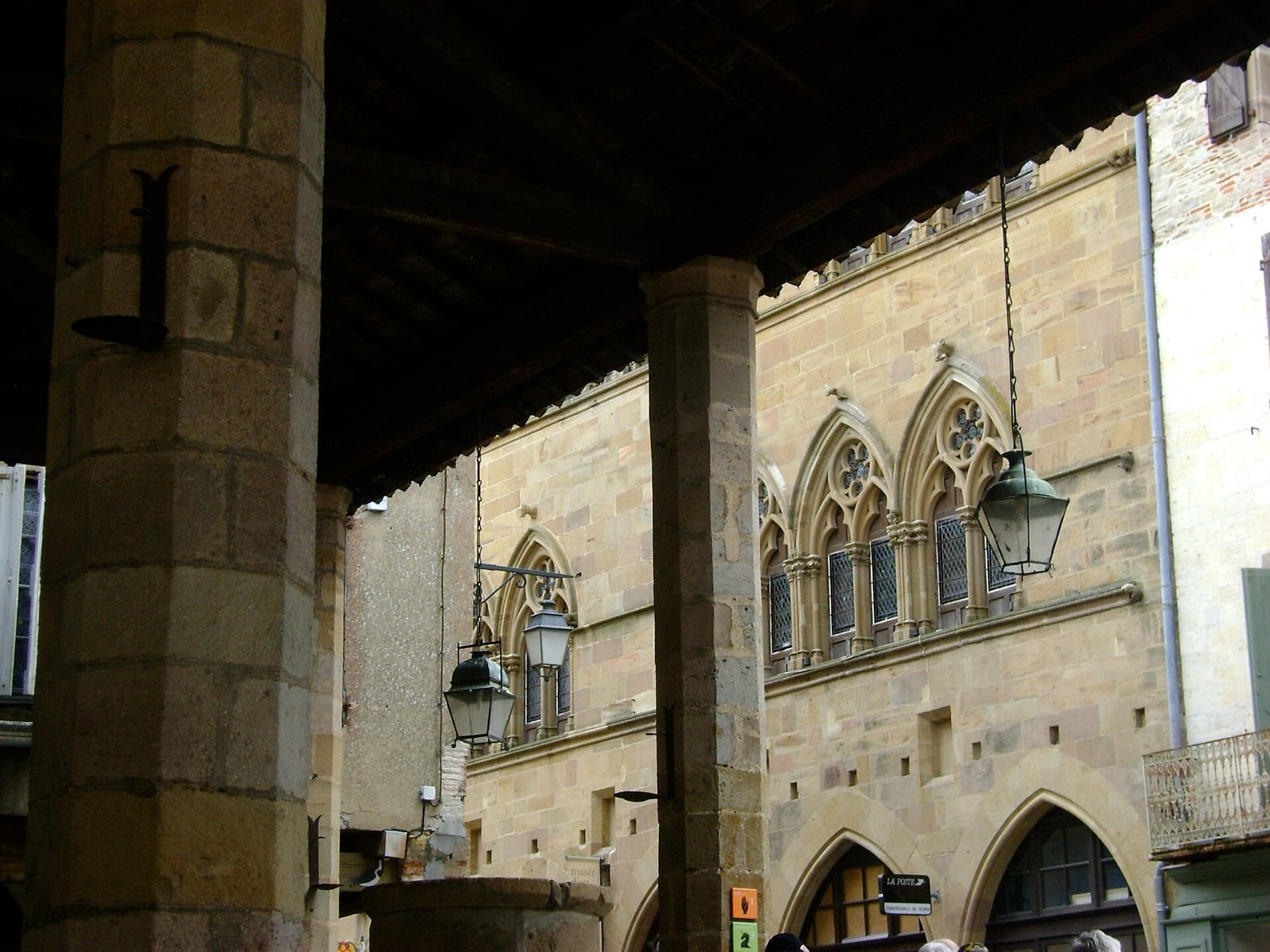 Façade de pierre à l’étage percée de baies gothiques géminées à arcs brisés et remplages en rosace, au-dessus d’une arcade à arc brisé, à Cordes-sur-Ciel.