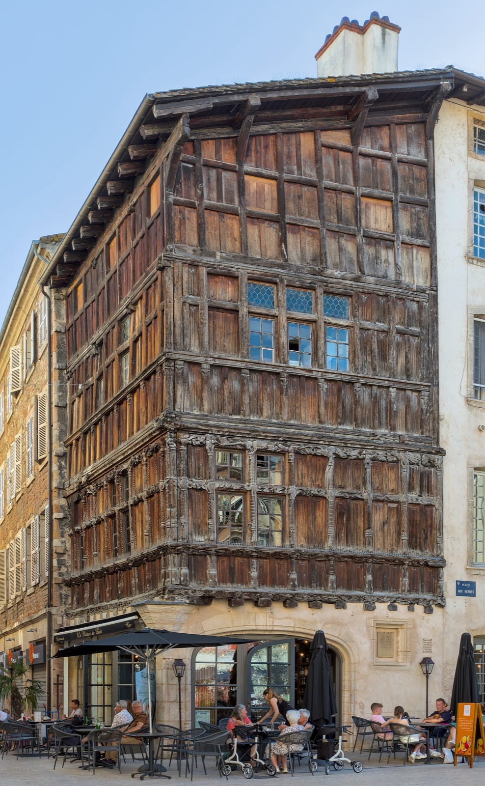 Maison d’angle à pans de bois de plusieurs étages en encorbellement, aux panneaux de bois sculptés et colonnettes, sur socle de pierre à porte en arc brisé, à Mâcon.