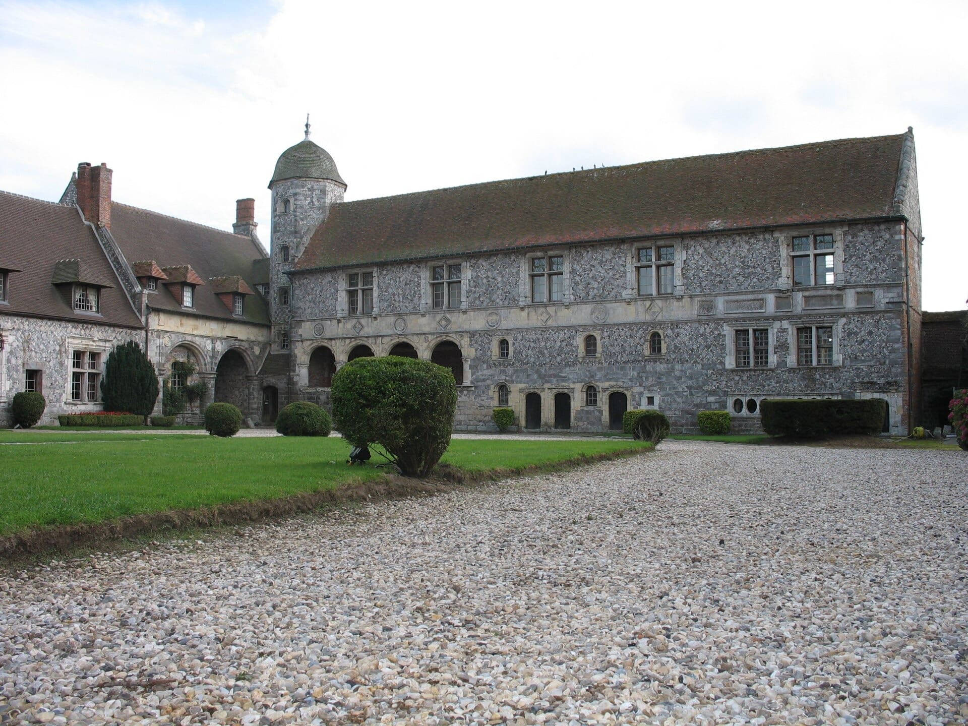 Longue façade Renaissance en damier de silex et de pierre, galerie à arcades au rez-de-chaussée, tourelle ronde en poivrière, autour d’une cour