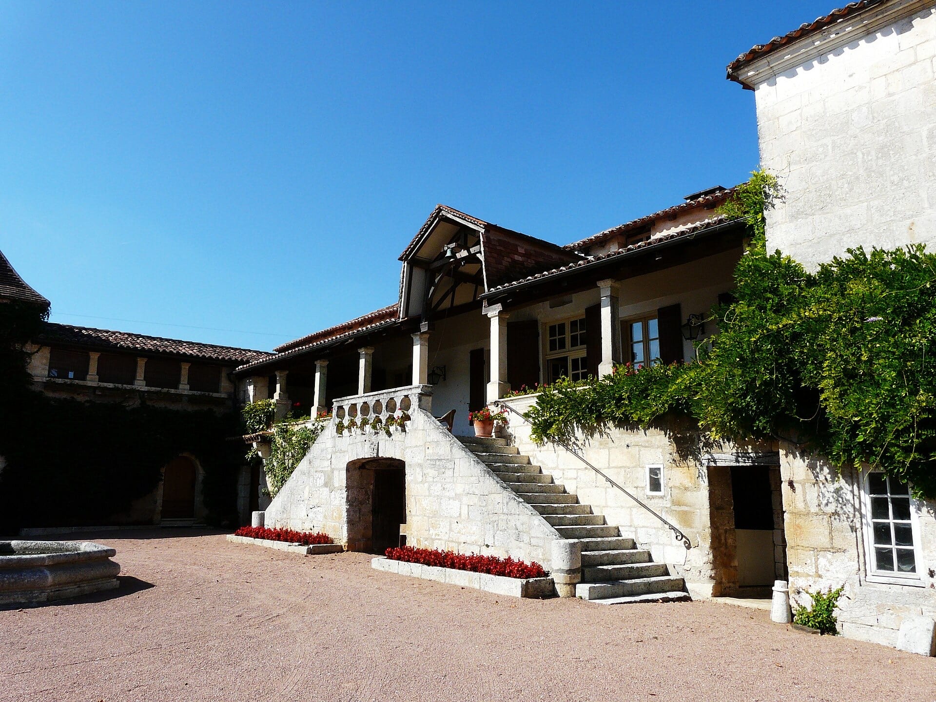 Logis de pierre calcaire claire à galerie sur colonnes desservie par un perron extérieur, cour avec puits